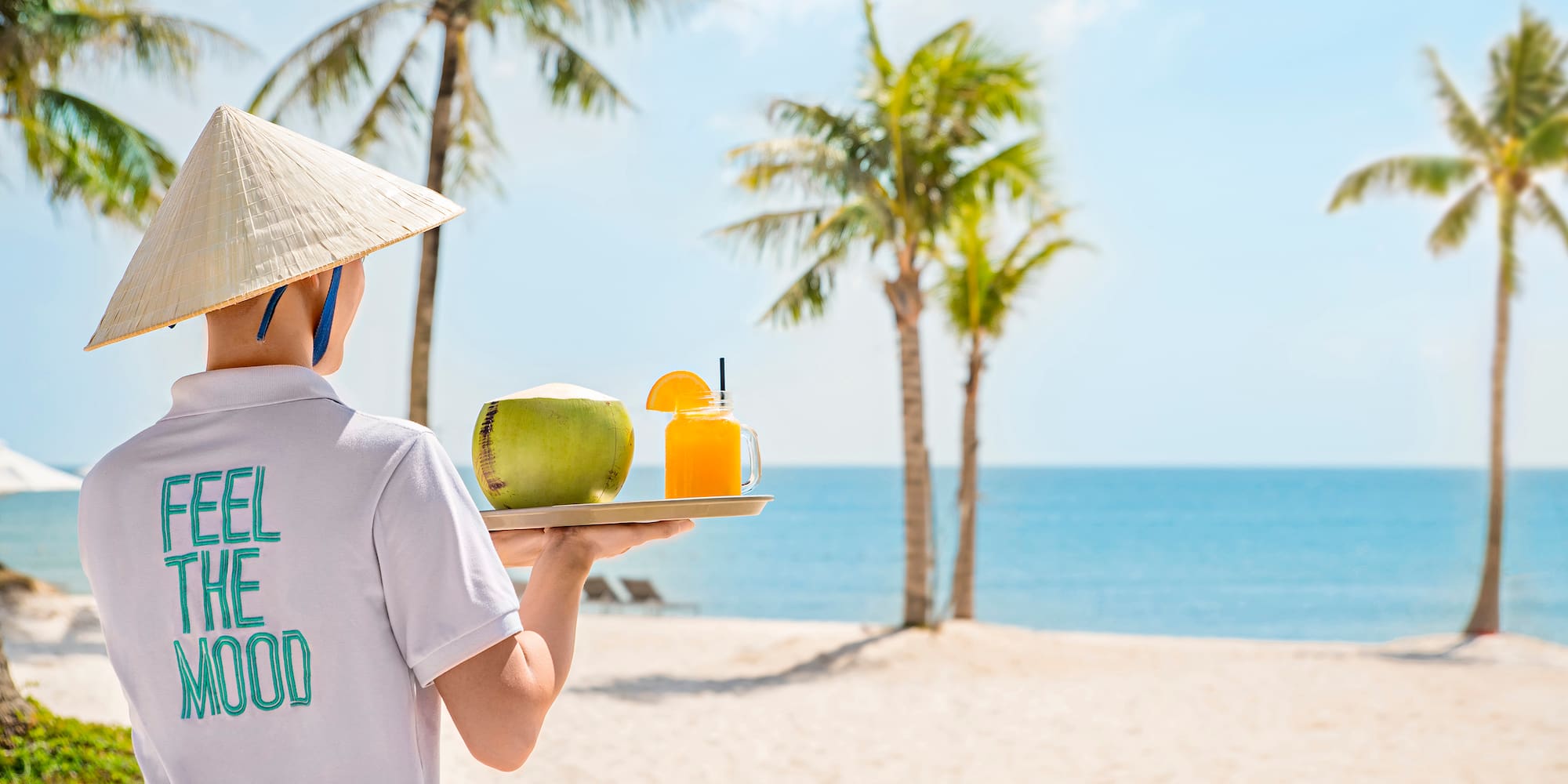 a person holding a tray with fruit and drink on a beach