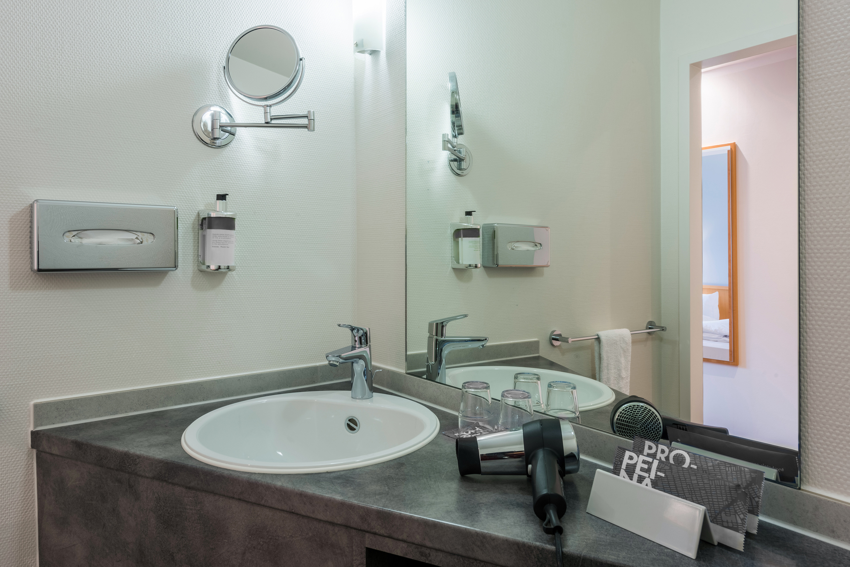 Modern hotel bathroom vanity with sink, mirror, hair dryer, and toiletries.