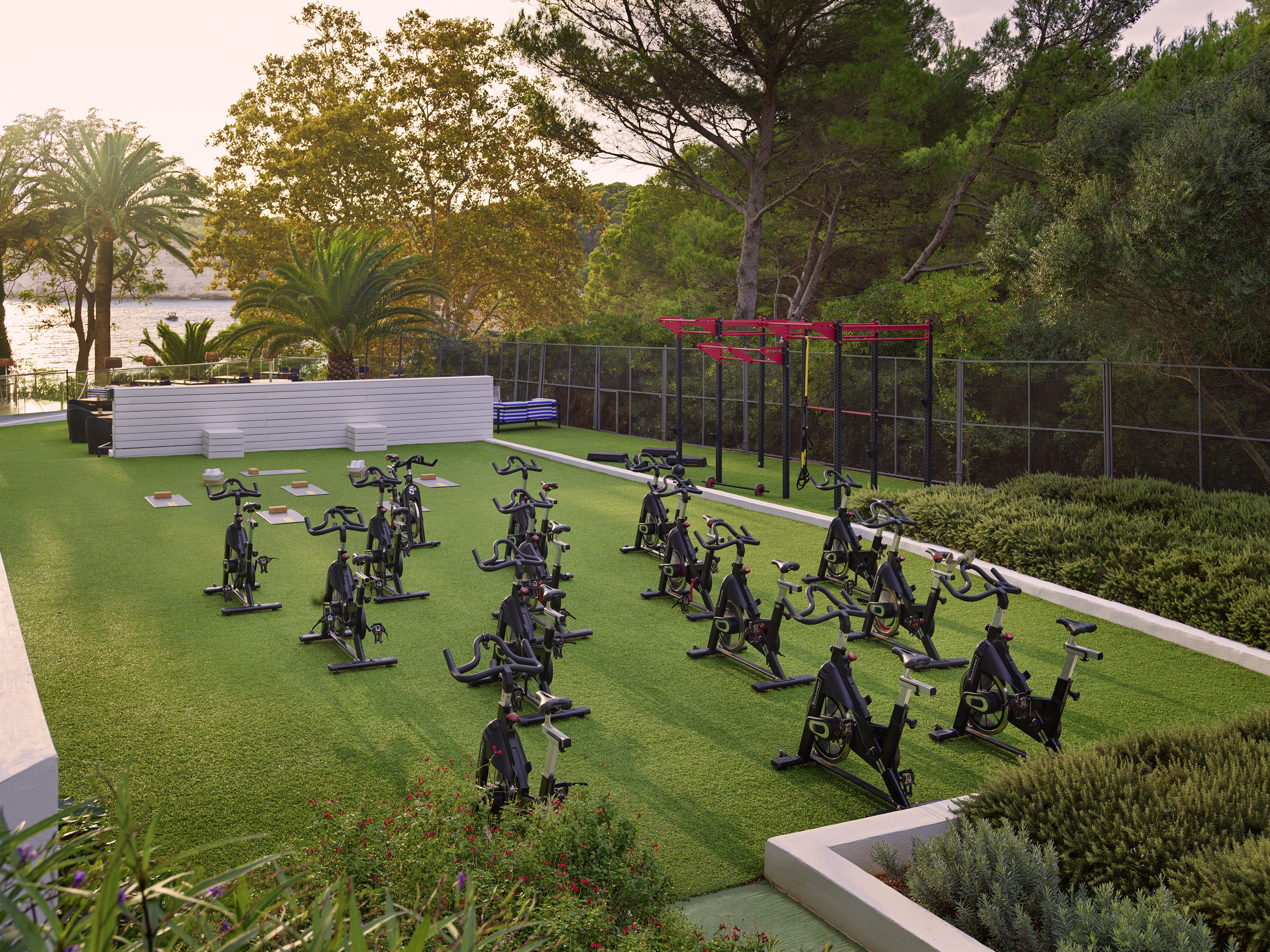 Outdoor spin class, exercise bikes on green turf with a fitness rig.