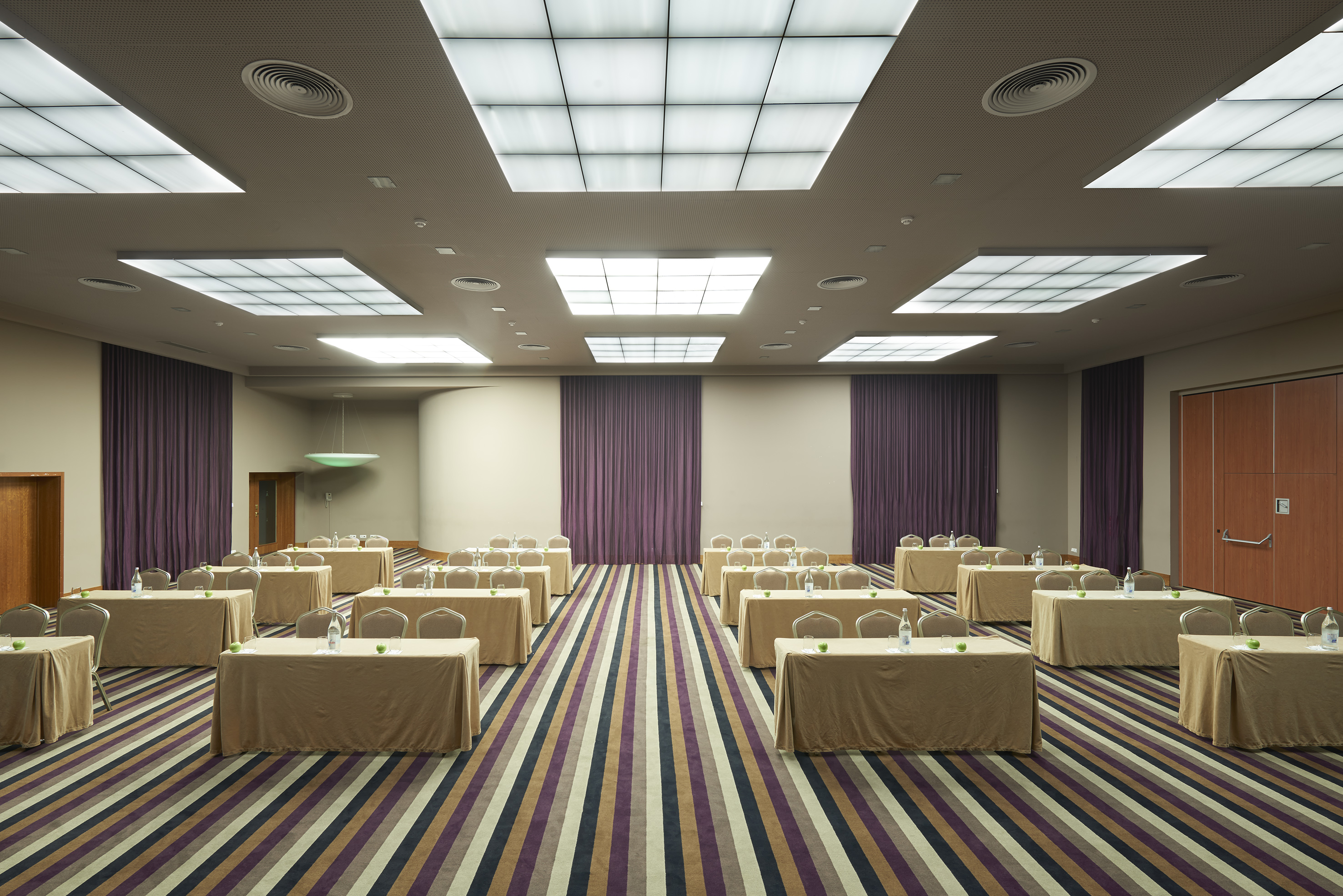 Meeting room with rows of tables, chairs, striped carpet, and purple curtains.