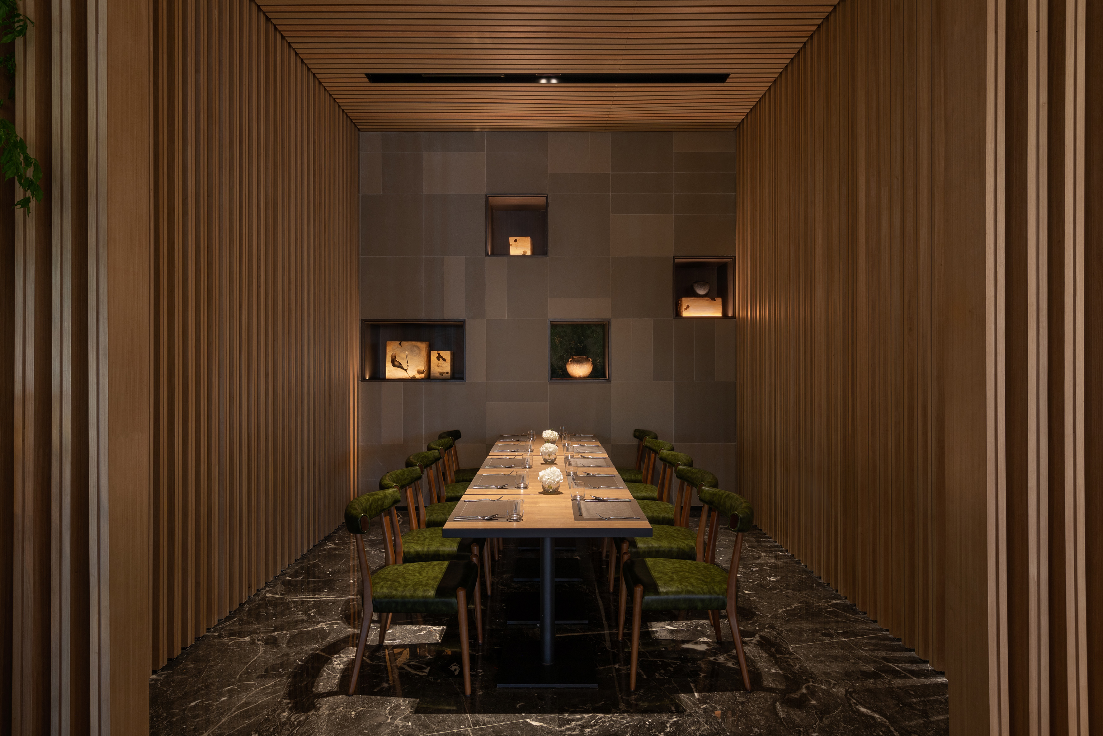 Modern private dining room with long wood table, green chairs, and slatted walls.