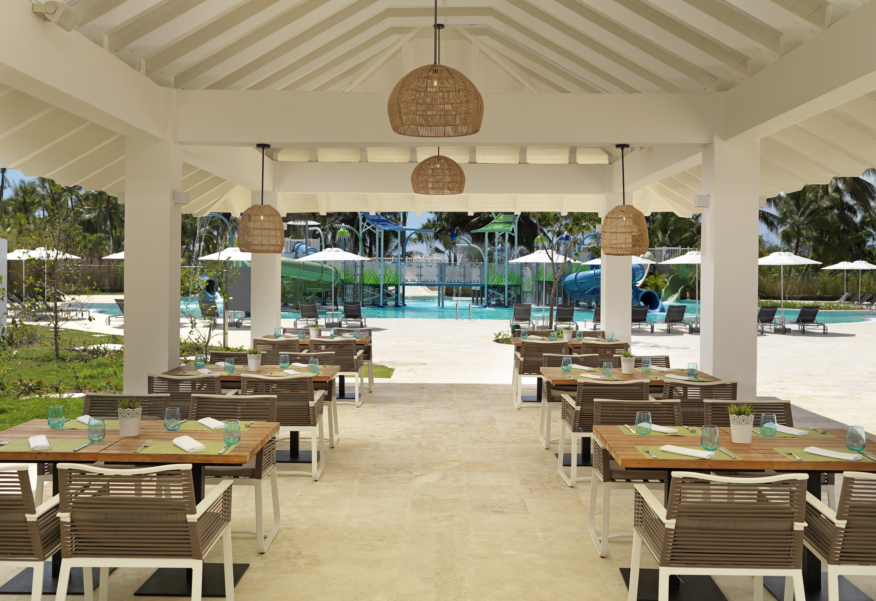 Tropical resort outdoor restaurant with water park, pool, and modern tables.