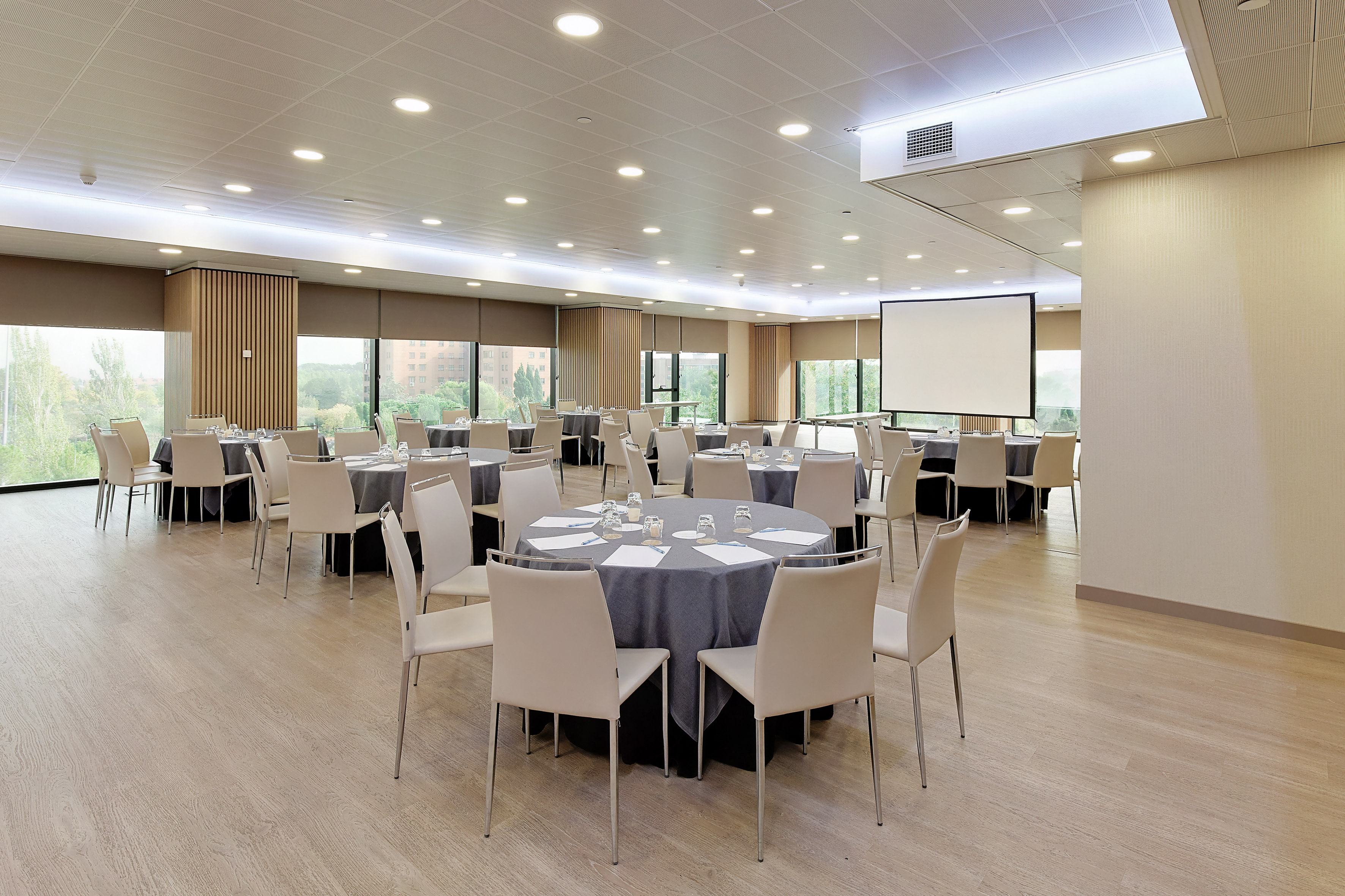 Bright conference room with round tables, light chairs, and projector screen.