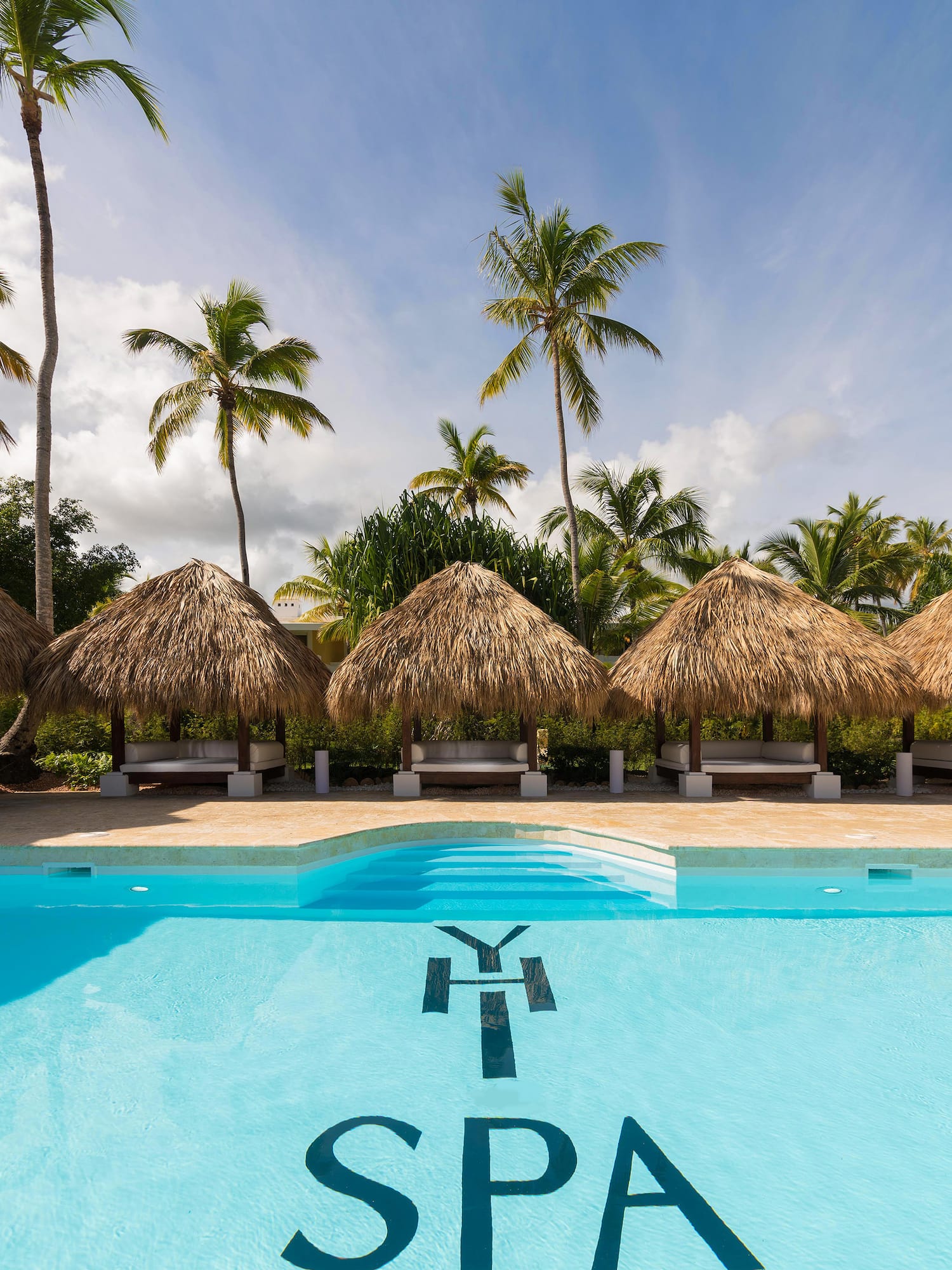 a pool with straw umbrellas and palm trees