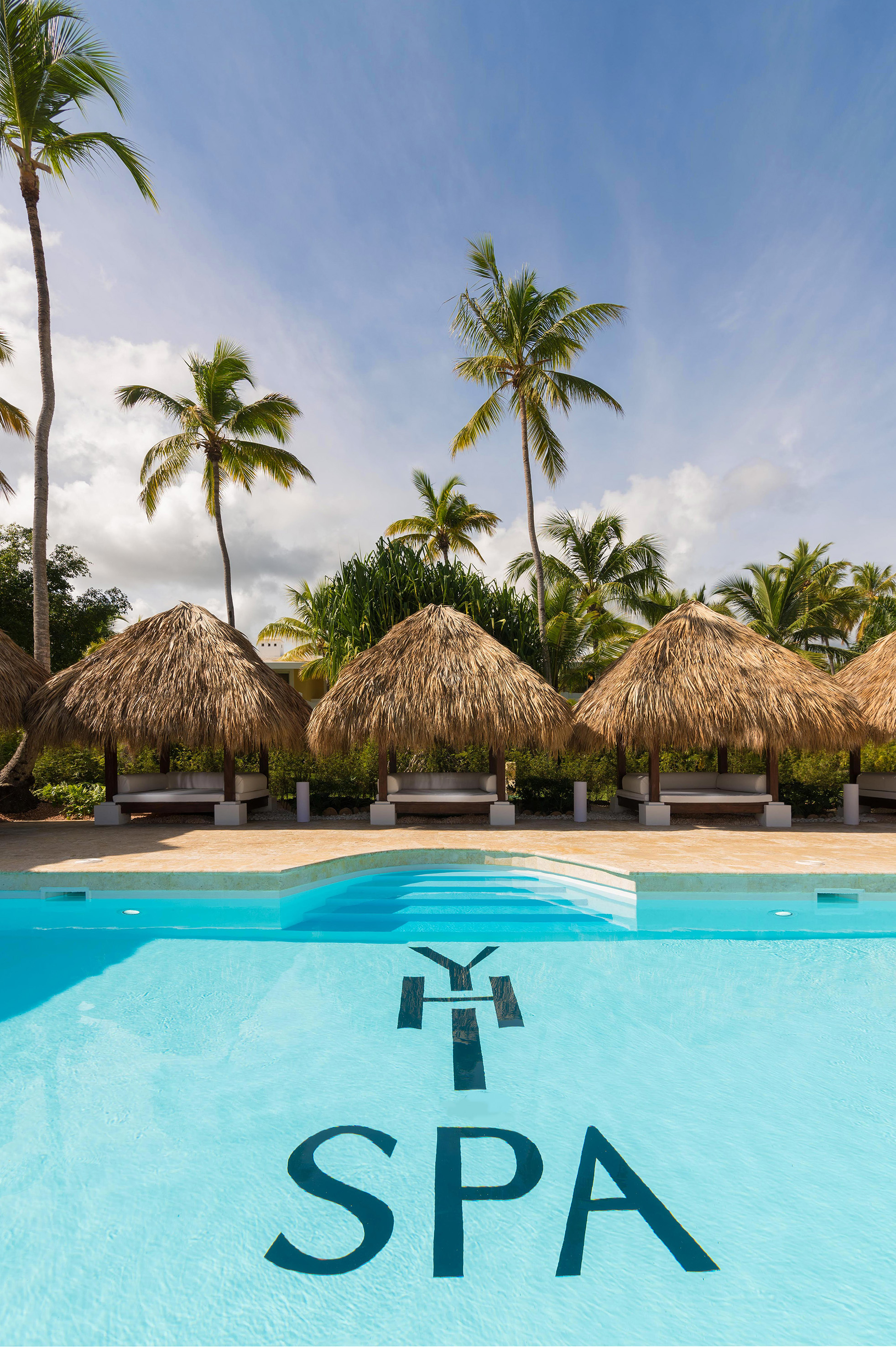 a pool with straw umbrellas and palm trees