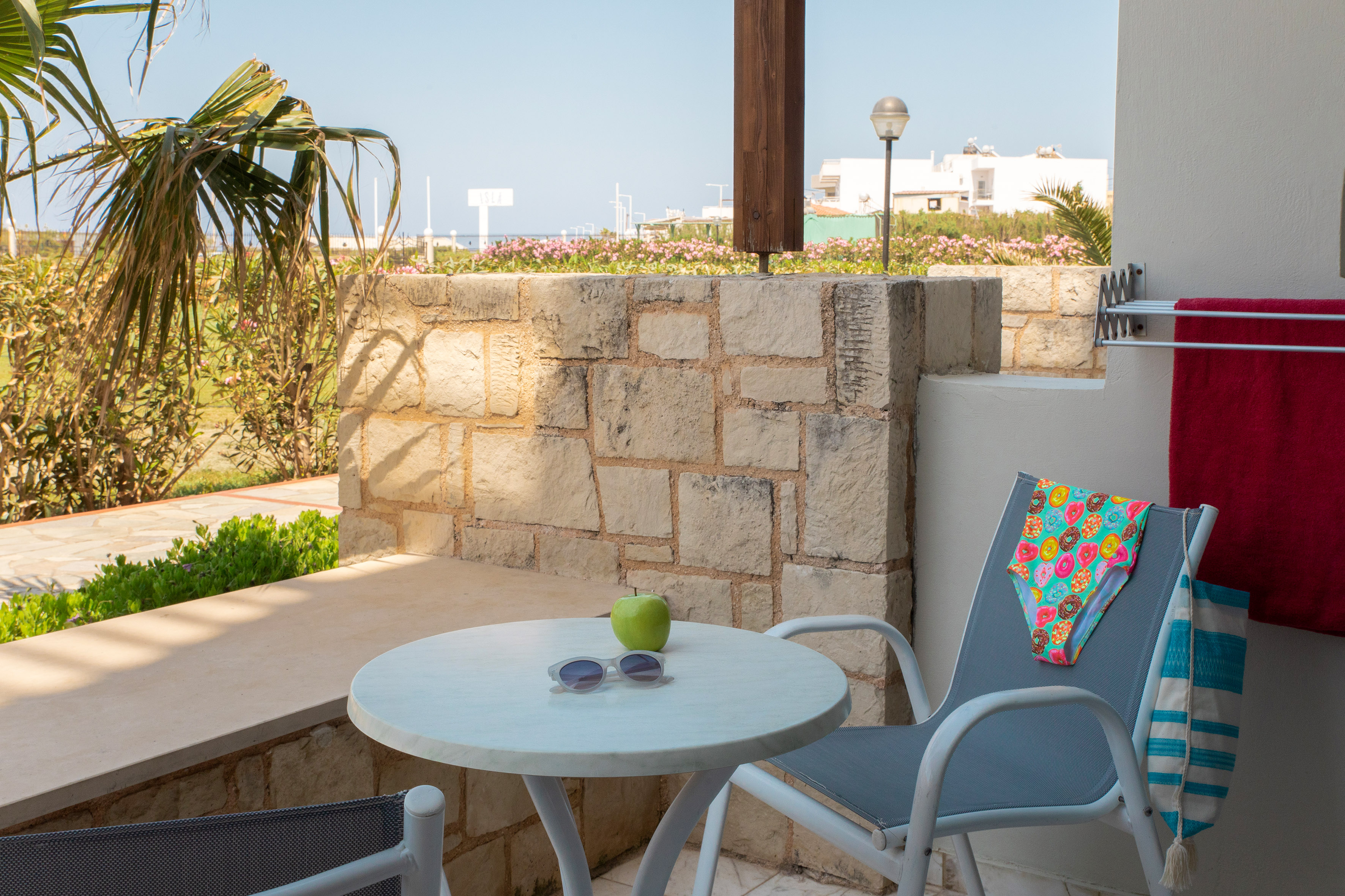 Sunny outdoor patio with stone wall, table, apple, sunglasses, and swimsuit.