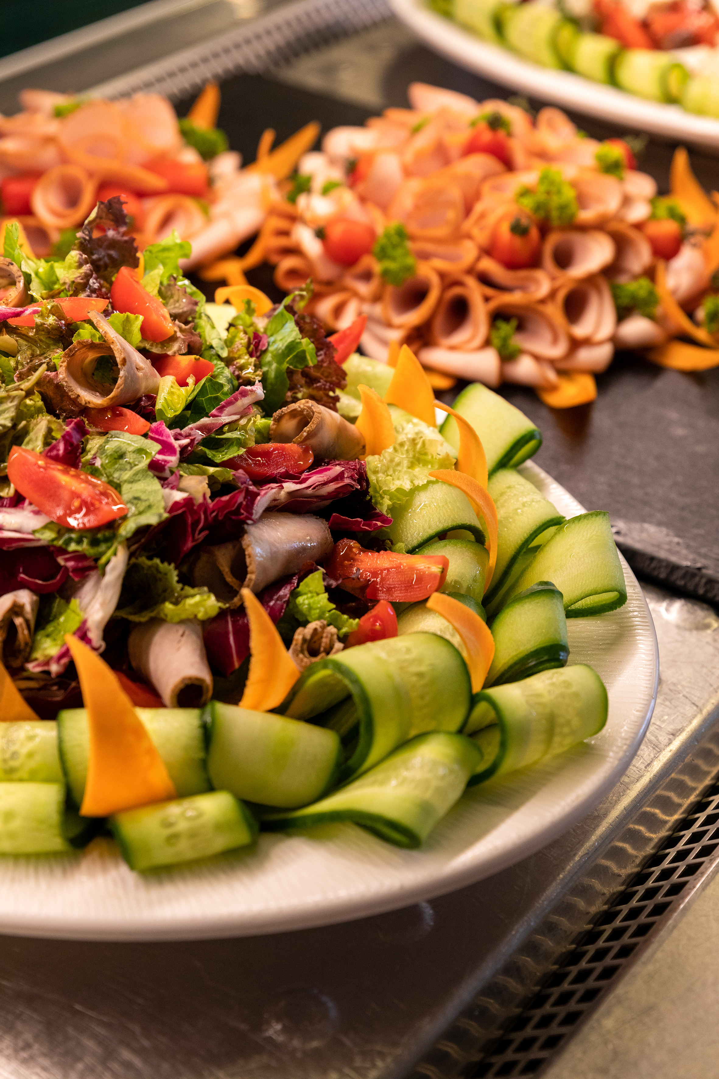 Fresh buffet salad with mixed greens, deli meat rolls, cucumber, and tomato.