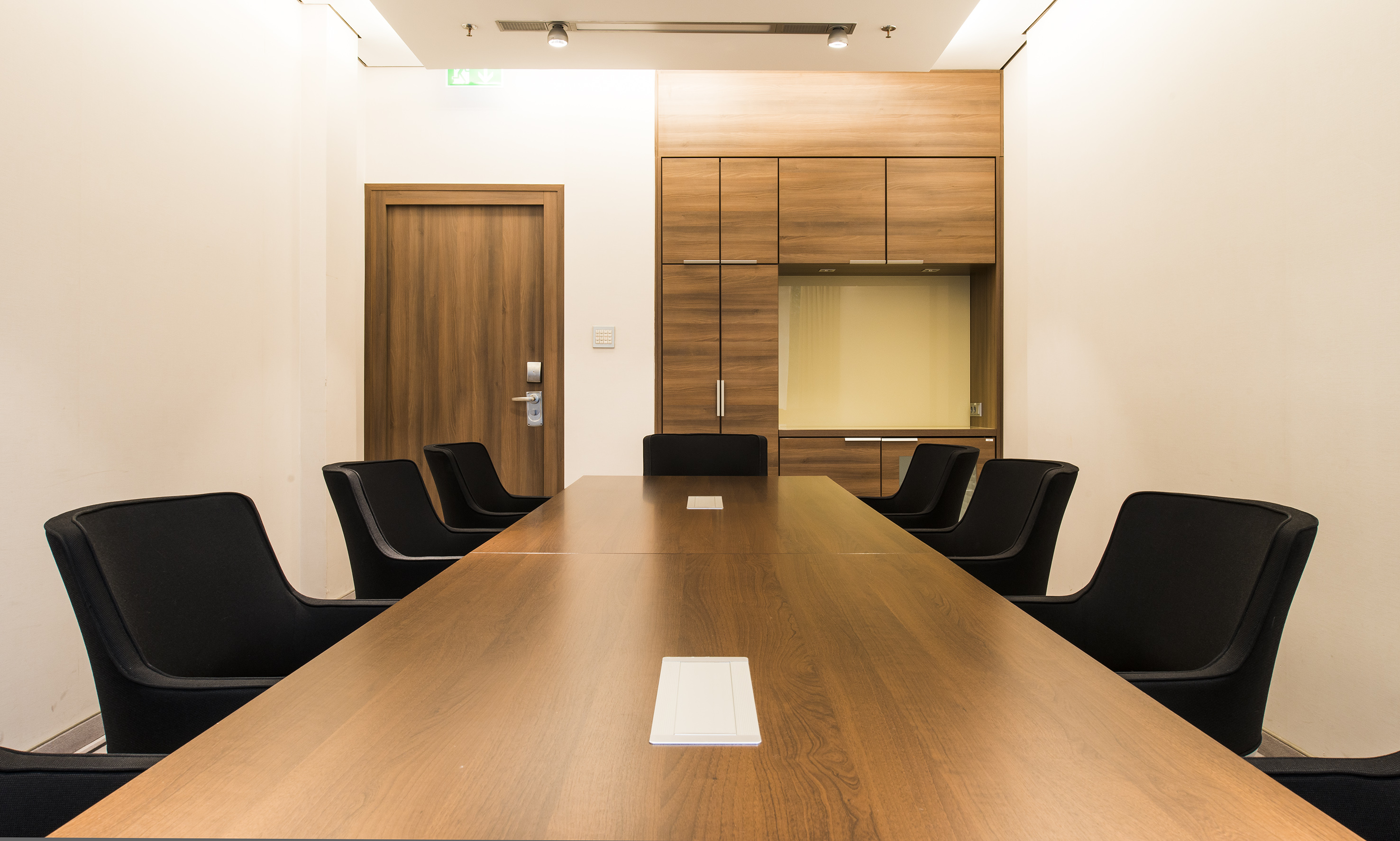 Modern meeting room with large wooden table, black chairs, and office cabinets.