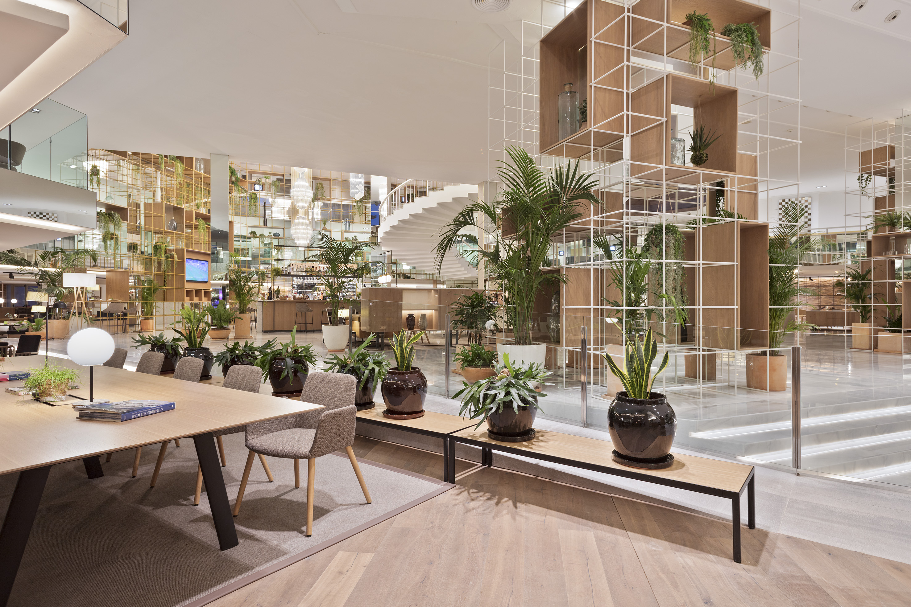 Modern biophilic lobby interior with lush plants, communal table, and spiral staircase.