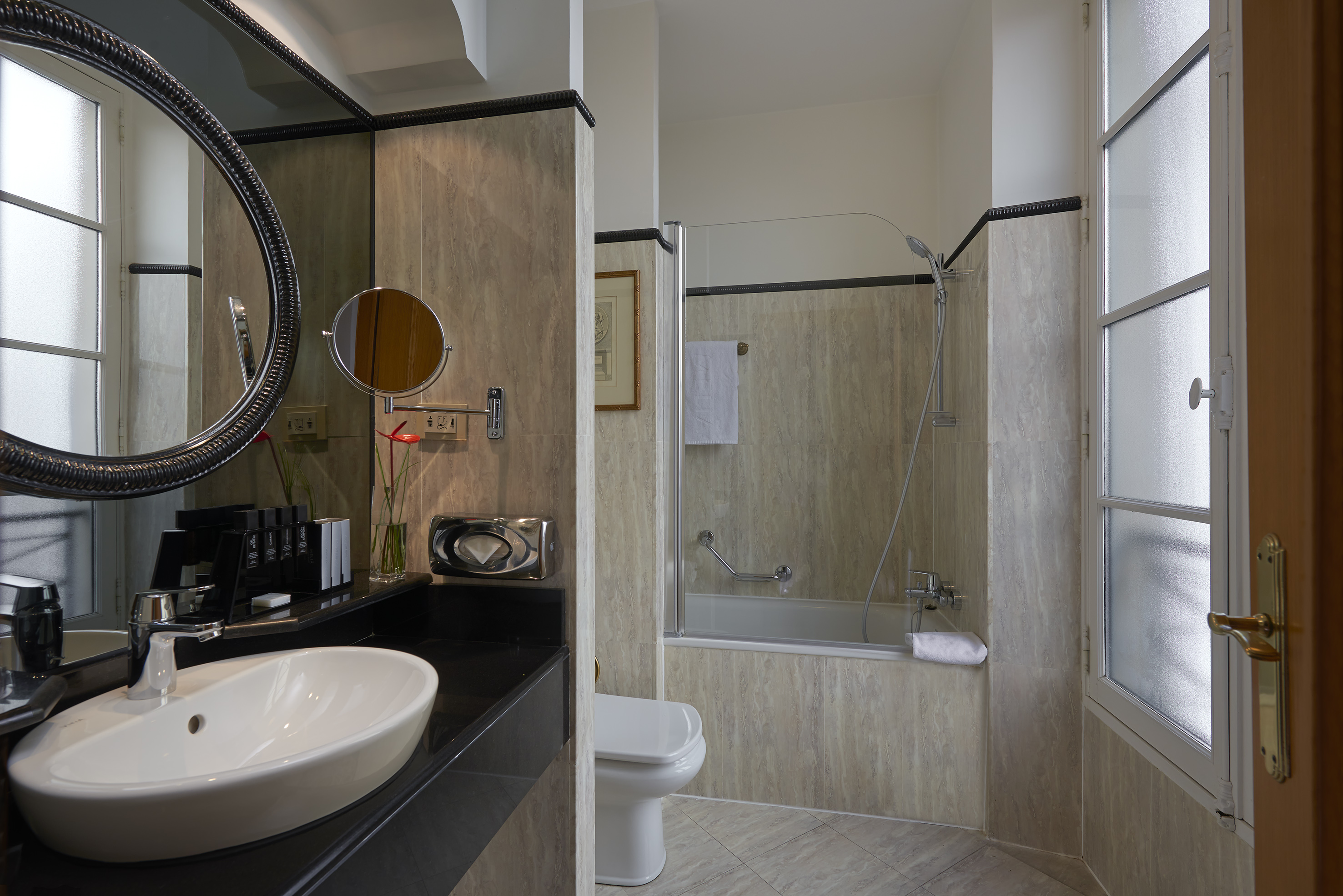 Modern hotel bathroom with white sink, ornate mirror, toilet, and shower tub.