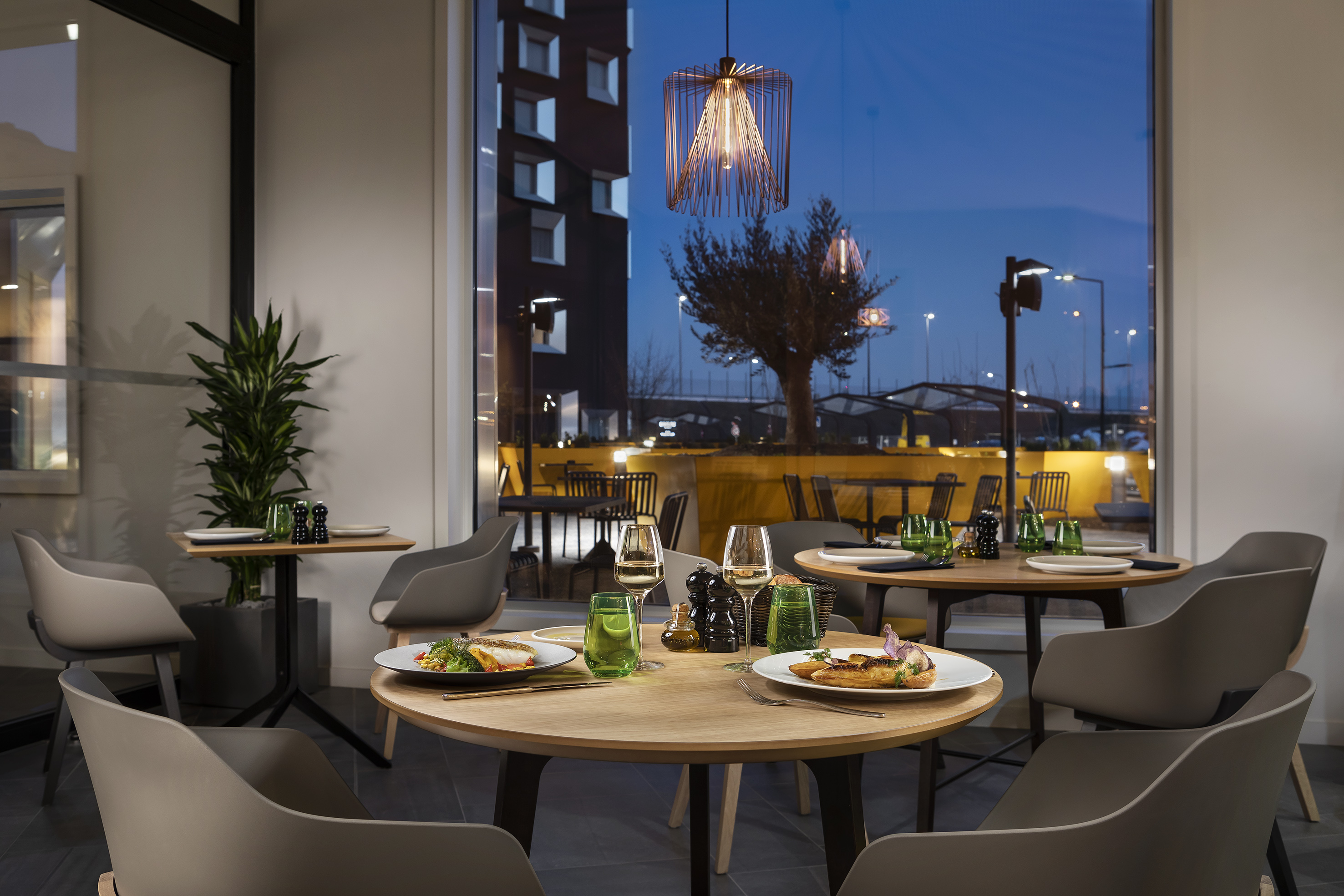 Modern restaurant interior with prepared tables, food, and evening city view.