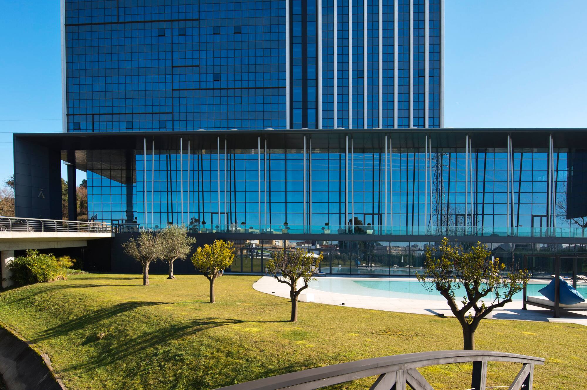 Meliã Braga hotel, modern glass building, garden, pool, and wooden bridge.