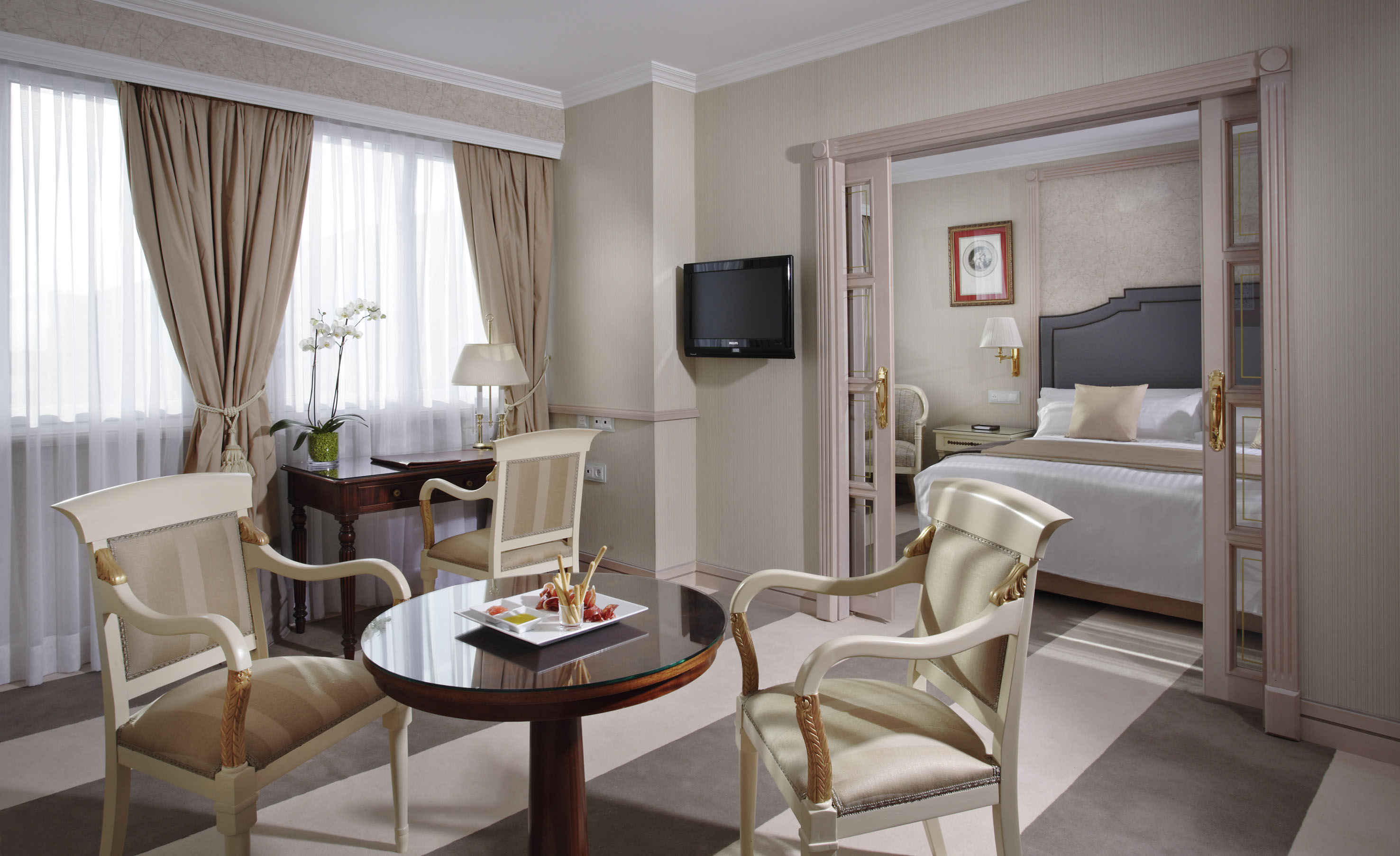 Elegant hotel suite with living room, desk, and connected bedroom.