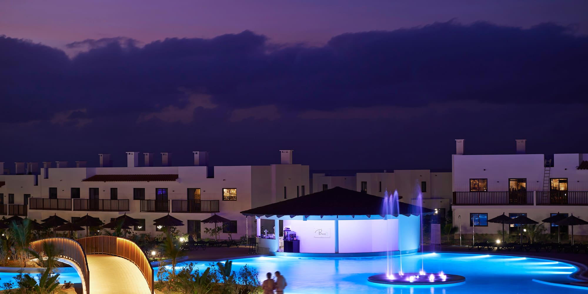 a pool with a fountain and buildings in the background