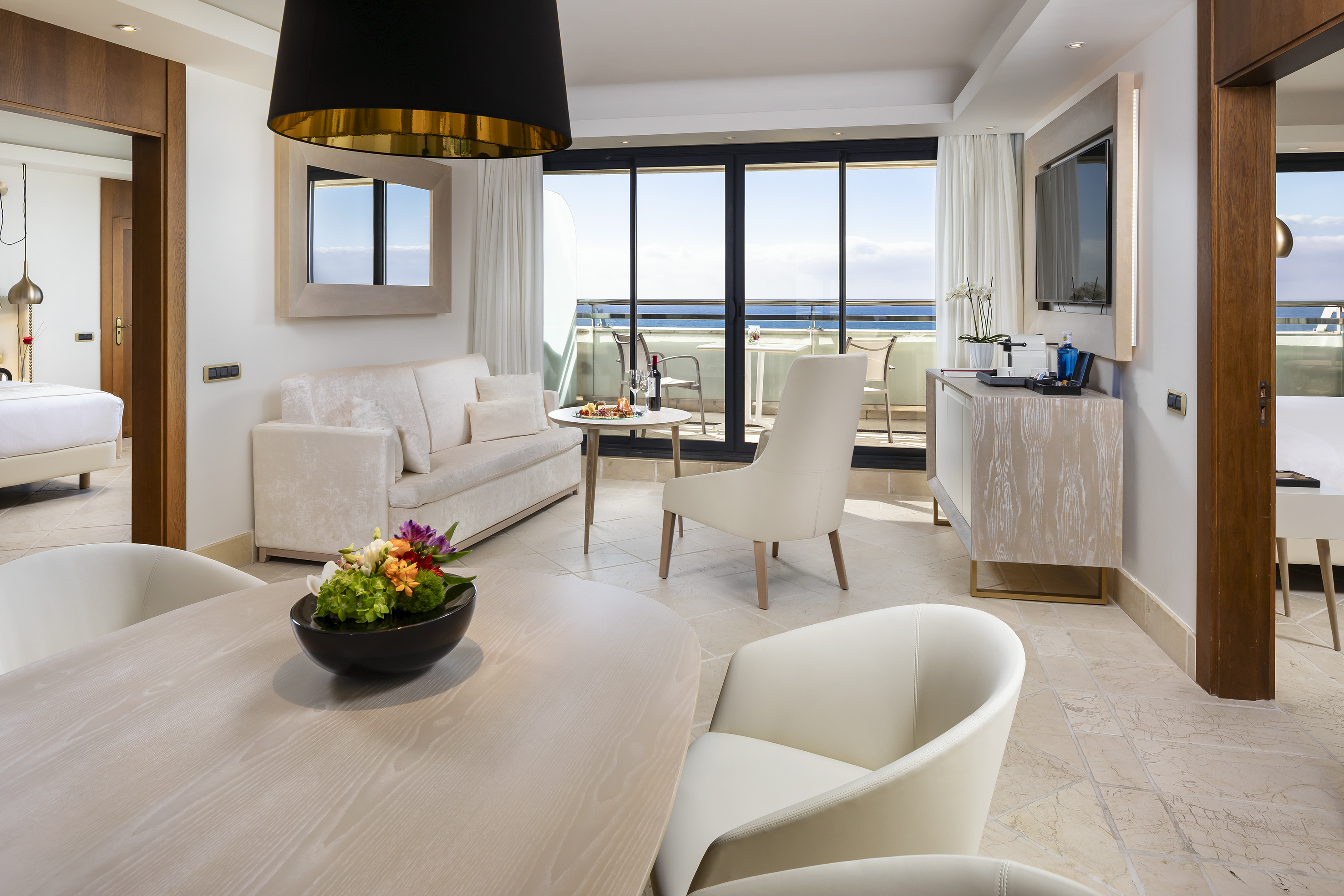Luxury hotel suite with ocean view balcony, dining area, and cream sofa.