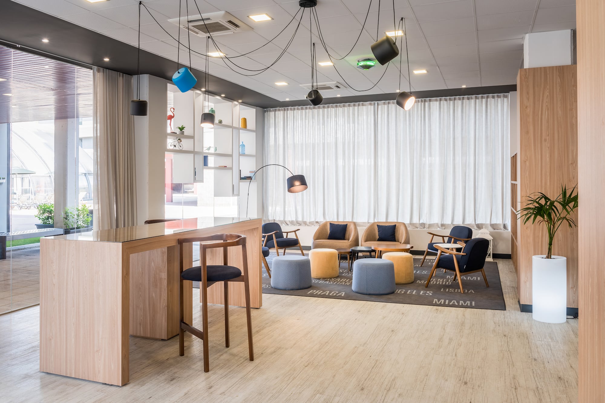 Modern hotel lounge with wooden bar, armchairs, colorful ottomans, pendant lights.