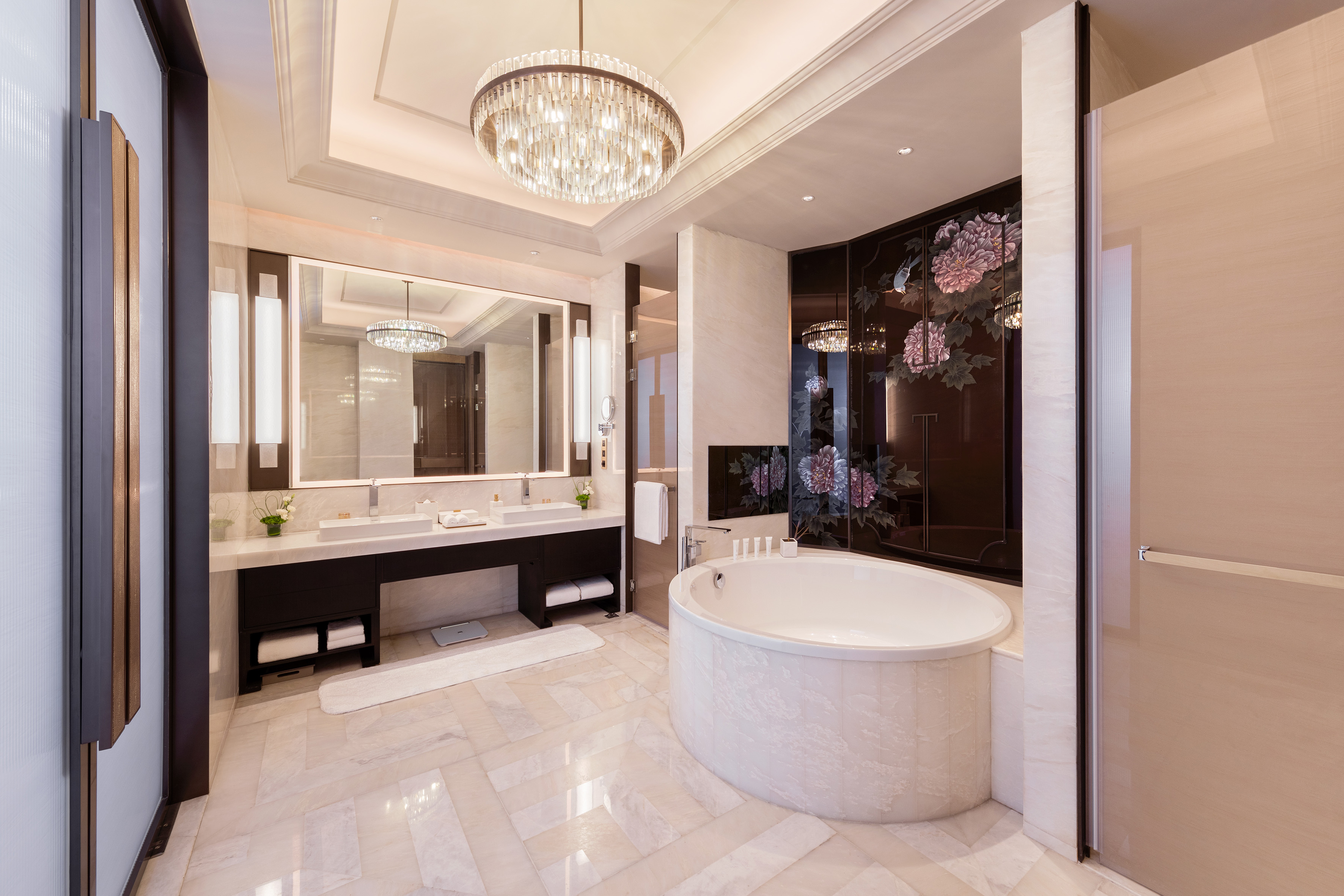 Luxury bathroom: crystal chandelier, double vanity, freestanding tub, floral decor.