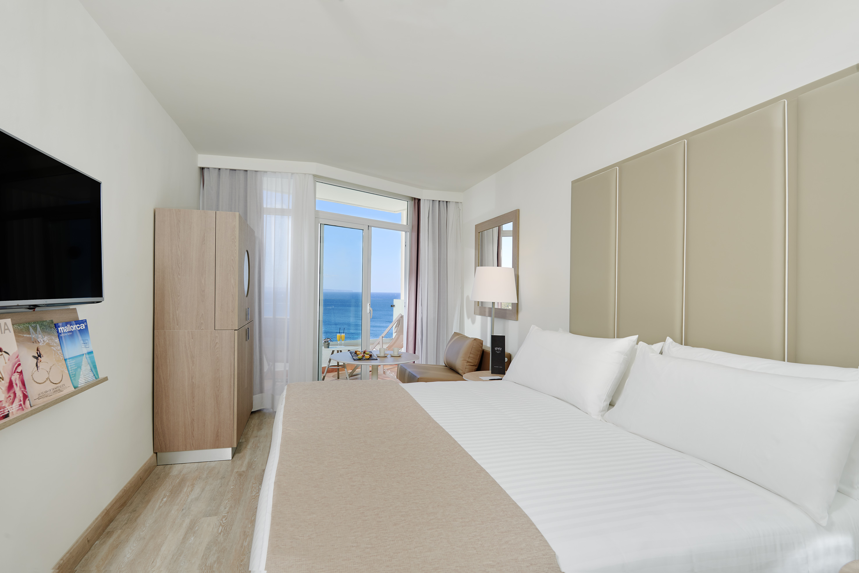 Hotel bedroom with sea view balcony, spacious bed, TV, and wardrobe.