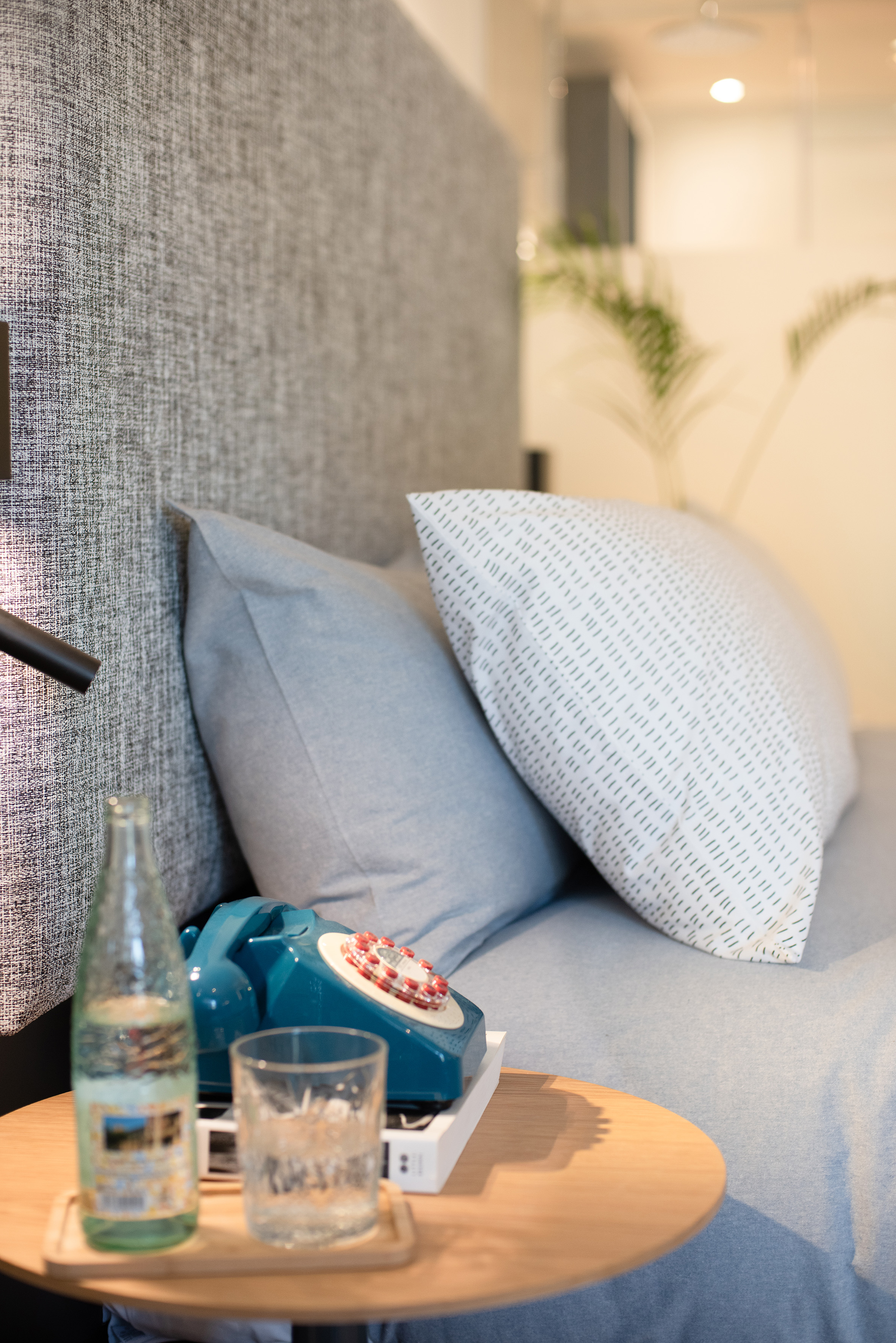 Turquoise retro rotary phone on bedside table by bed with pillows.
