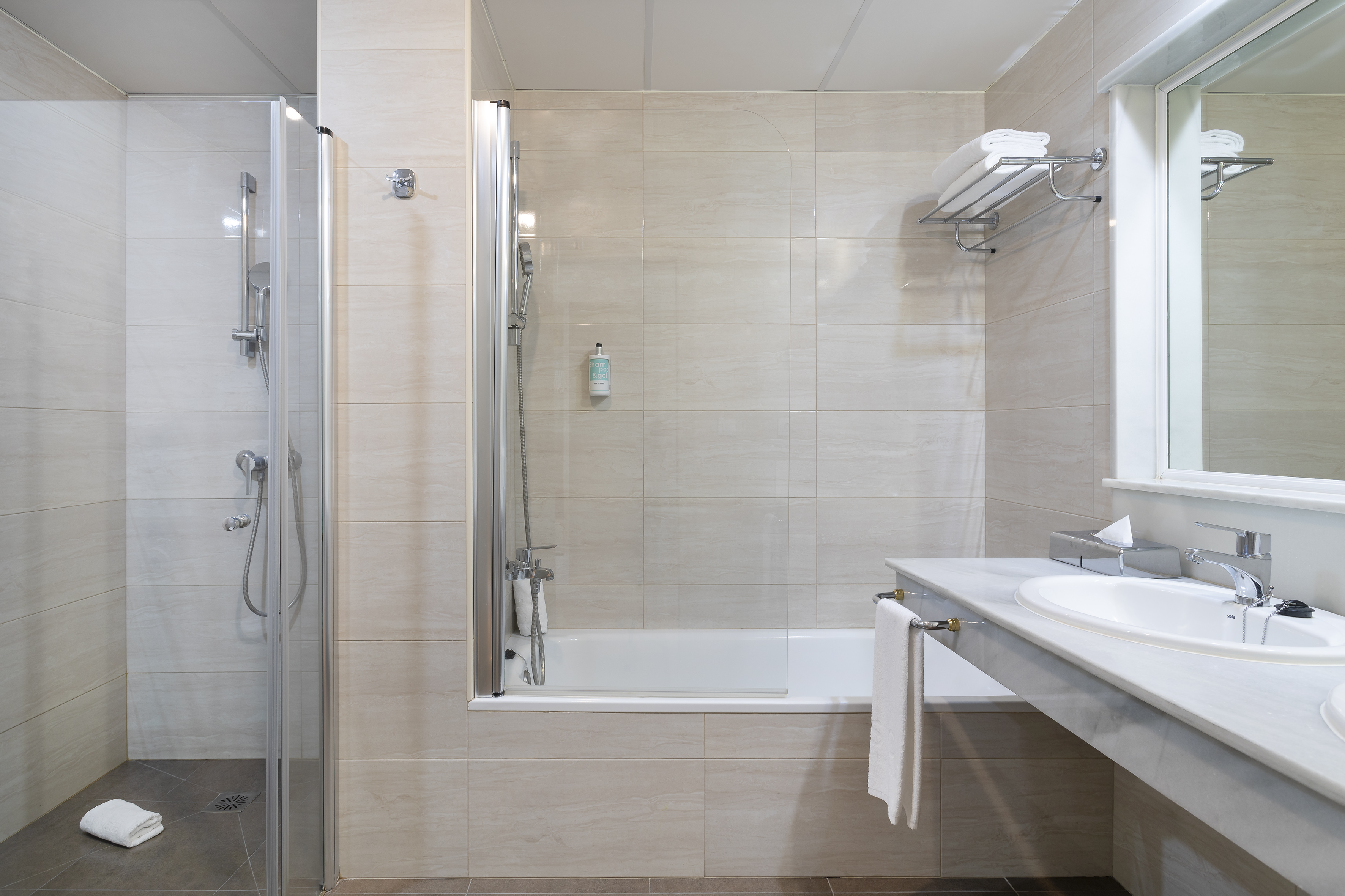 Hotel bathroom with walk-in shower, bathtub, and sink on light tiled walls.