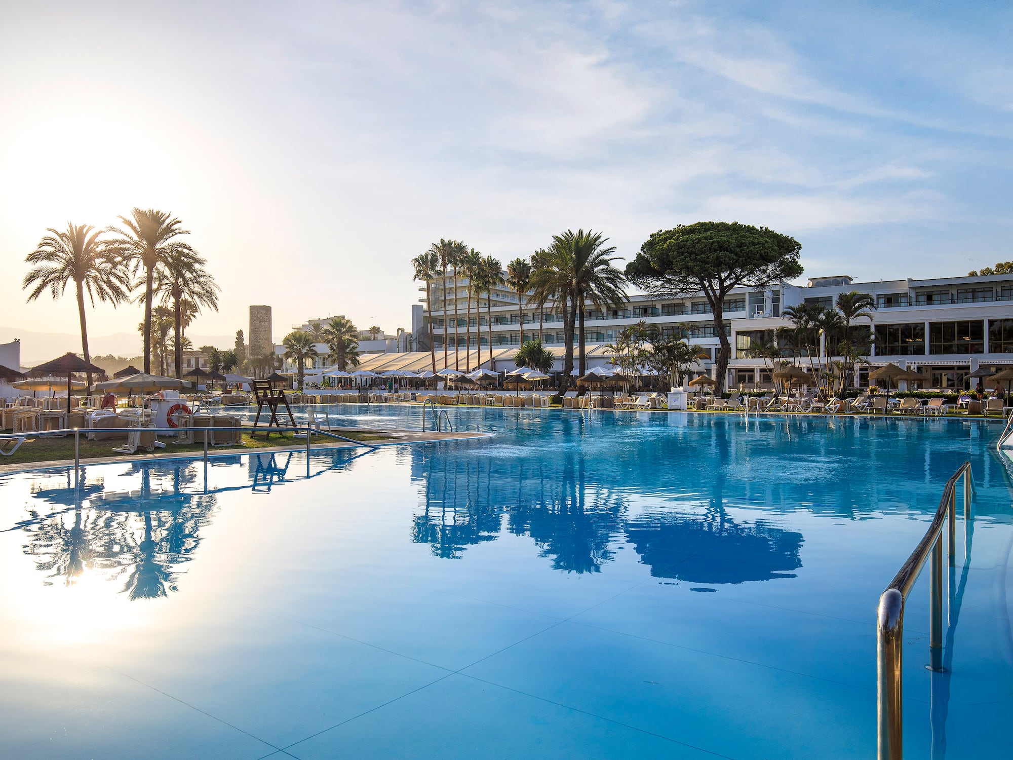 Luxury resort swimming pool with hotel and palm trees on a sunny day.