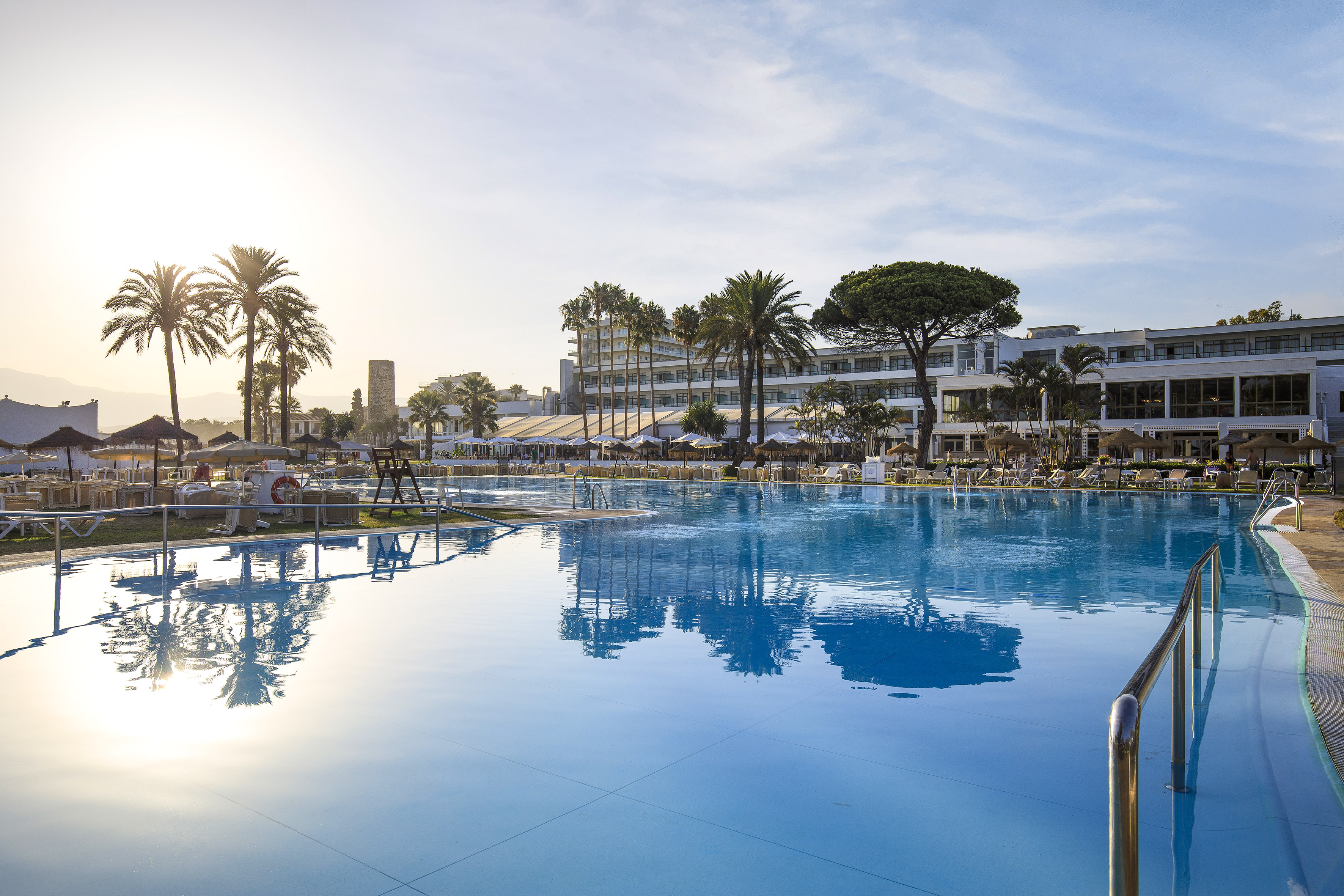 Luxury resort swimming pool with hotel and palm trees on a sunny day.