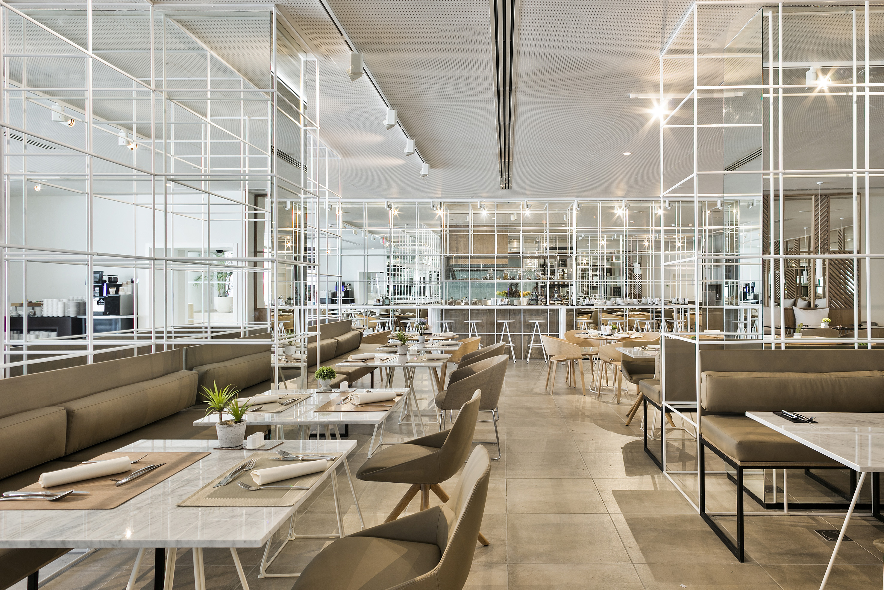 Bright modern restaurant interior, white grid, marble tables, beige banquettes.