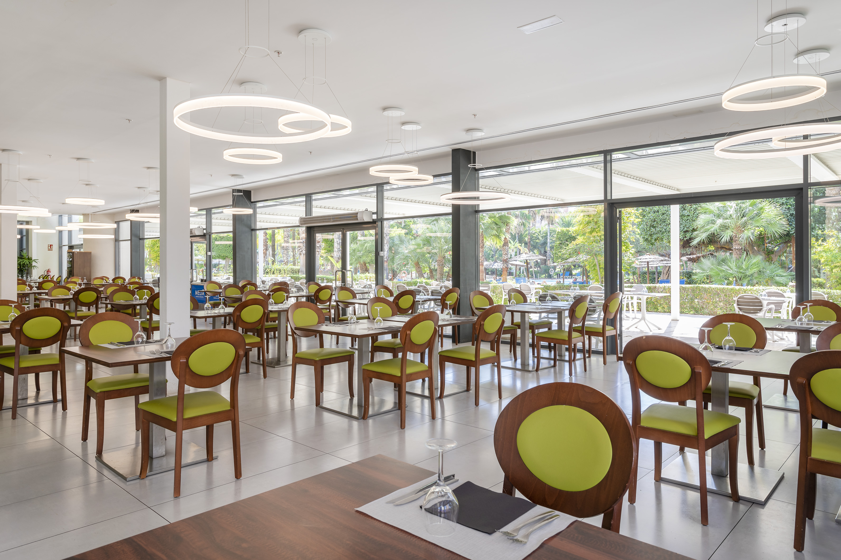 Bright modern restaurant with green chairs and tropical garden views.