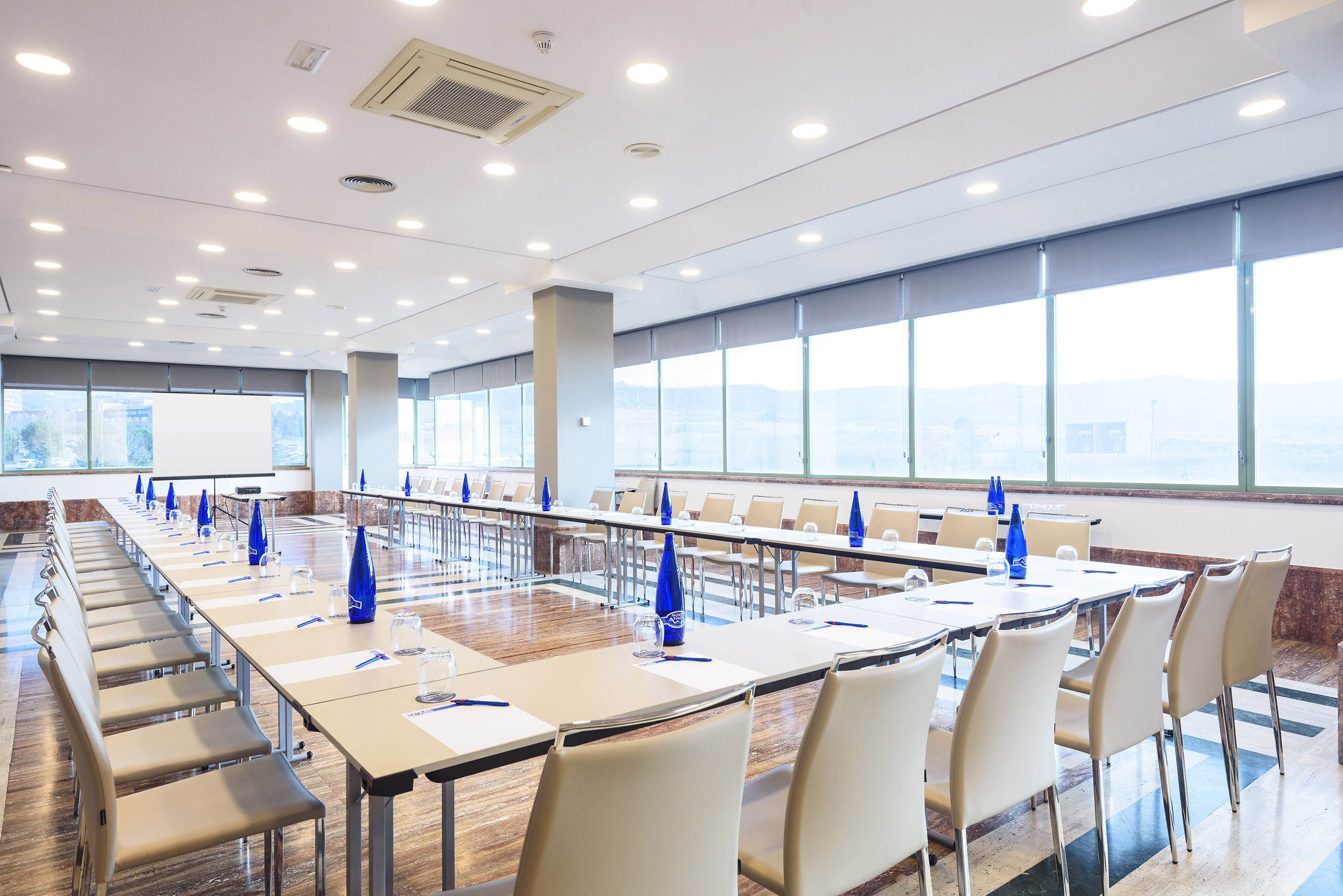 Modern U-shaped meeting room with tables, chairs, projection screen, and large windows.
