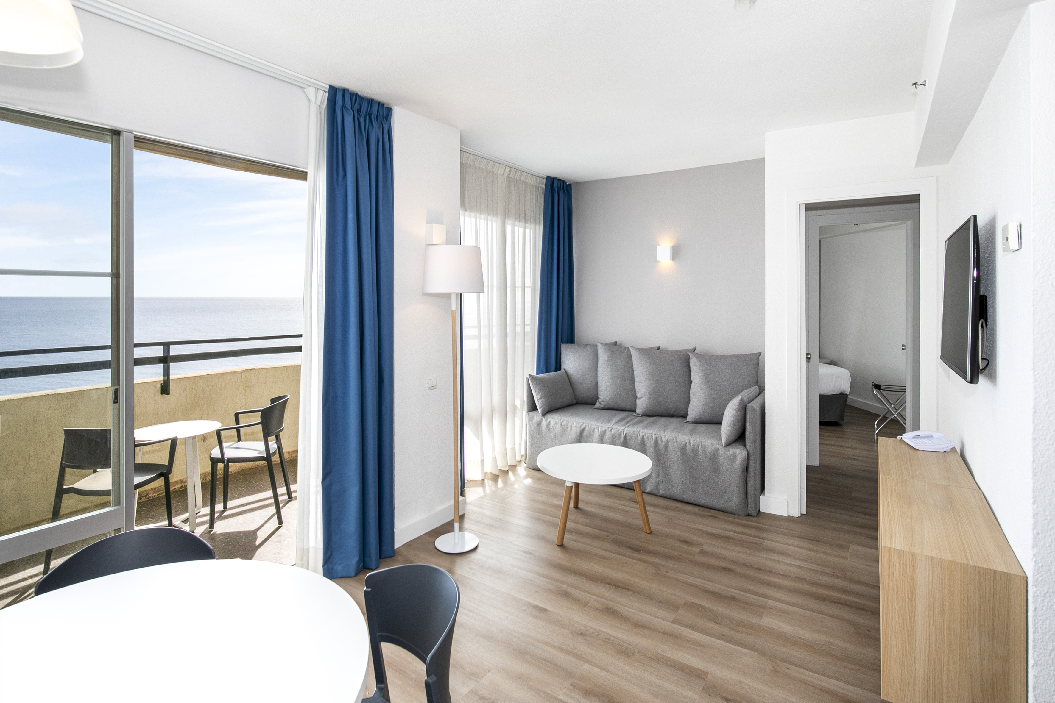 Modern apartment living room with ocean view balcony, gray sofa, and dining area.