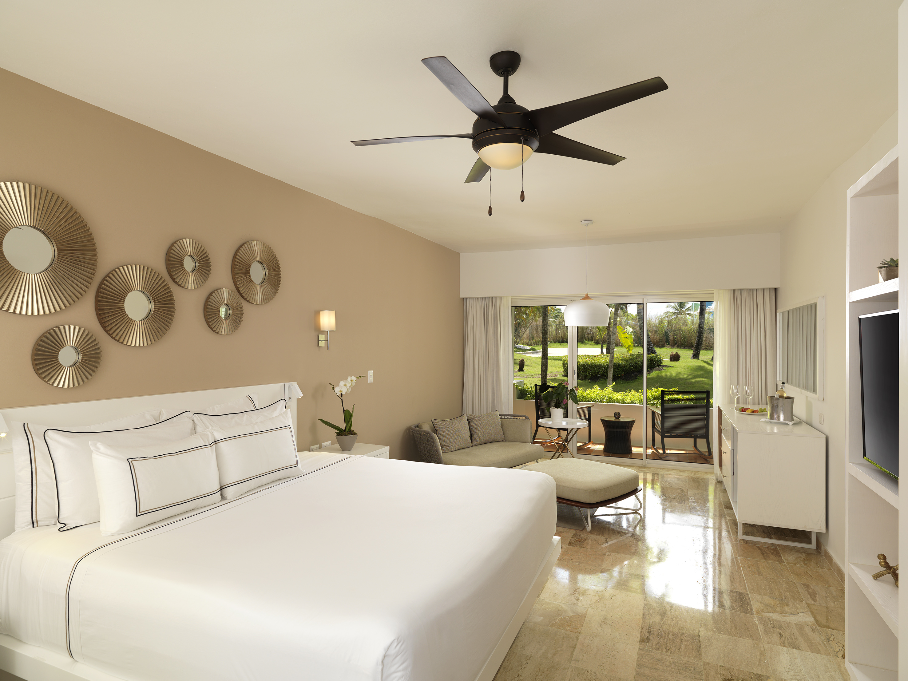 Luxury hotel room with king bed, sofa, private patio, and lush garden view.