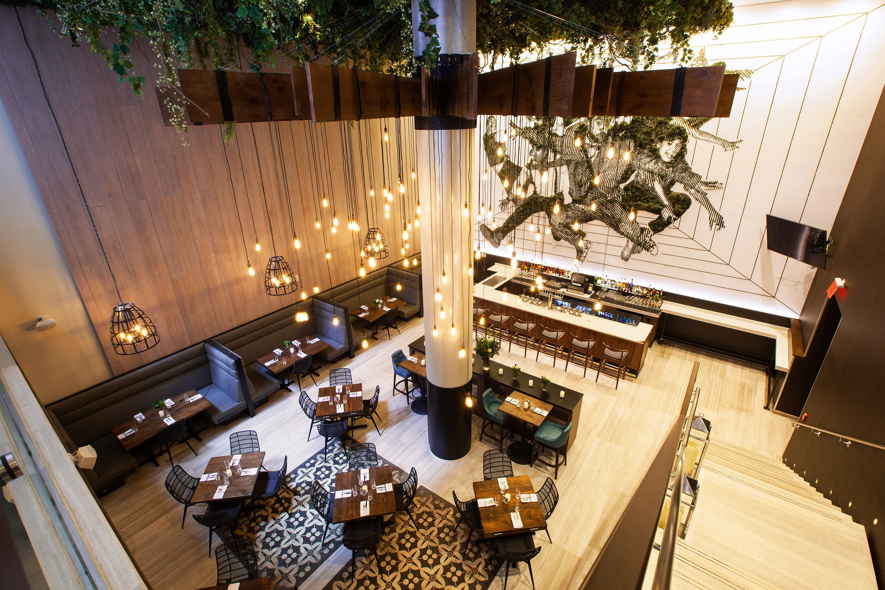 Modern restaurant interior: bar, dining tables, hanging lights, and wall mural.