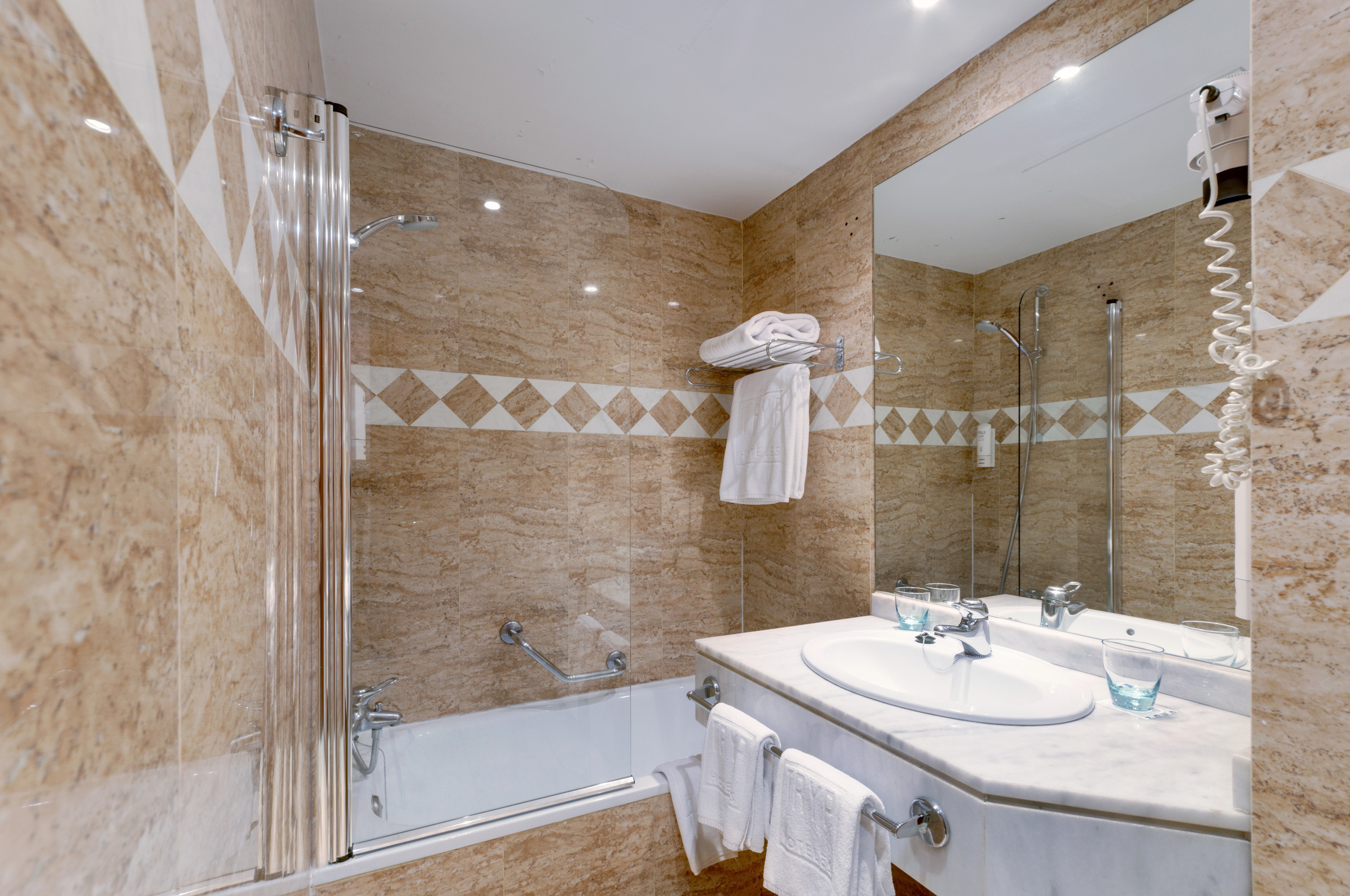 Hotel bathroom with beige marble tiles, bathtub, shower, sink, and mirror.