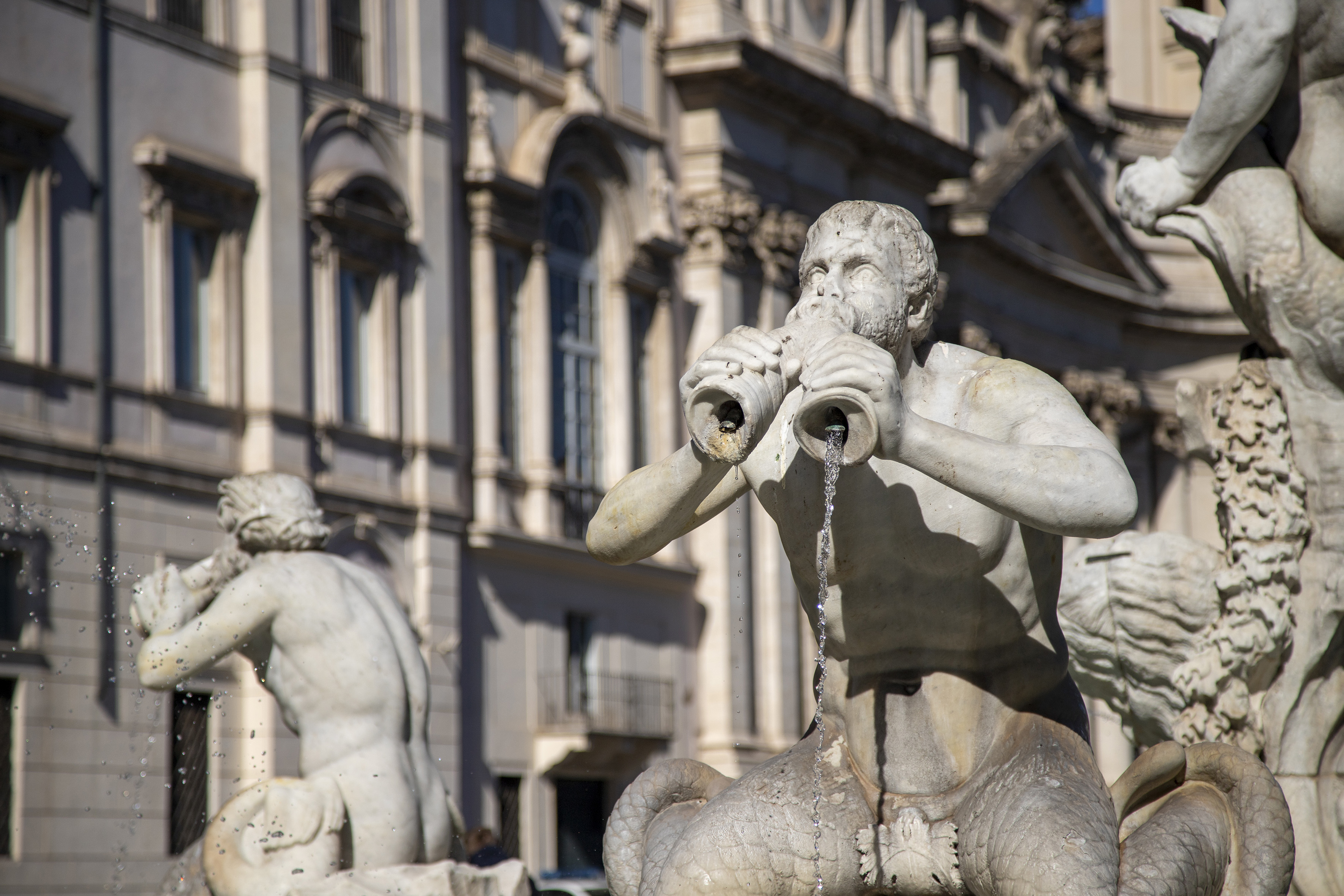 Marble Triton statue spouting water from shells at a historic Roman fountain.
