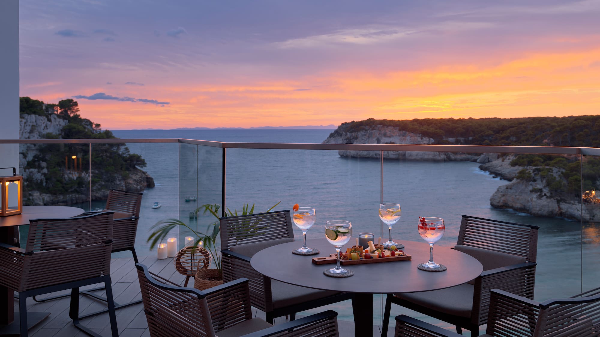 a table with wine glasses and food on it with a view of the ocean