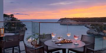a table with wine glasses and food on it with a view of the ocean