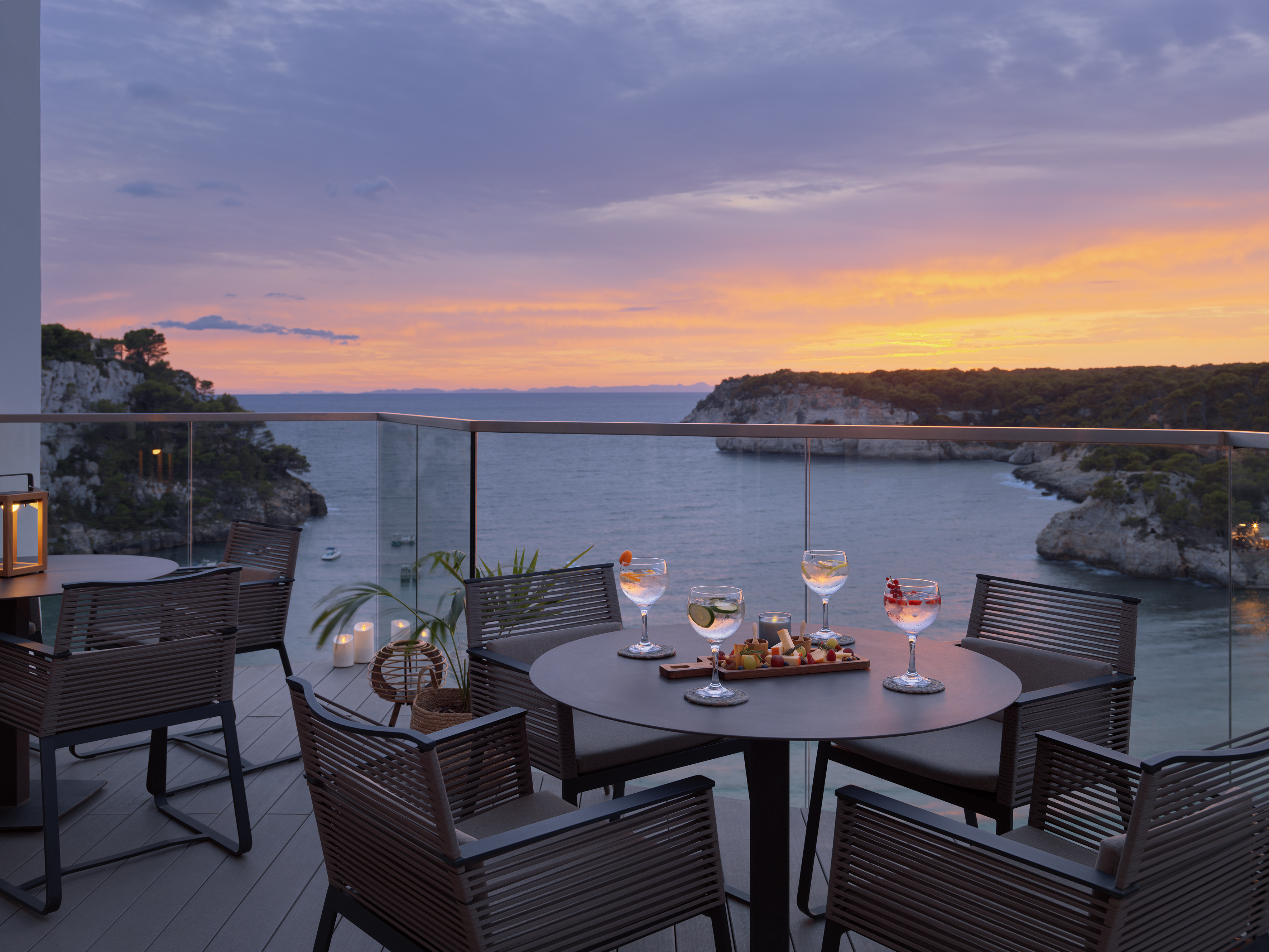 Sunset cocktails and snacks on a balcony overlooking a sea bay.