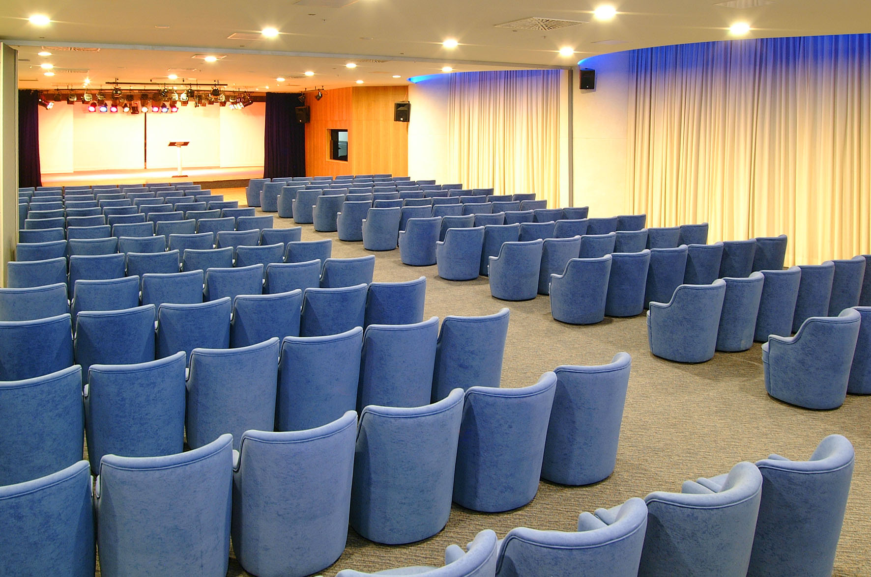 Modern conference hall with blue upholstered chairs and illuminated stage.
