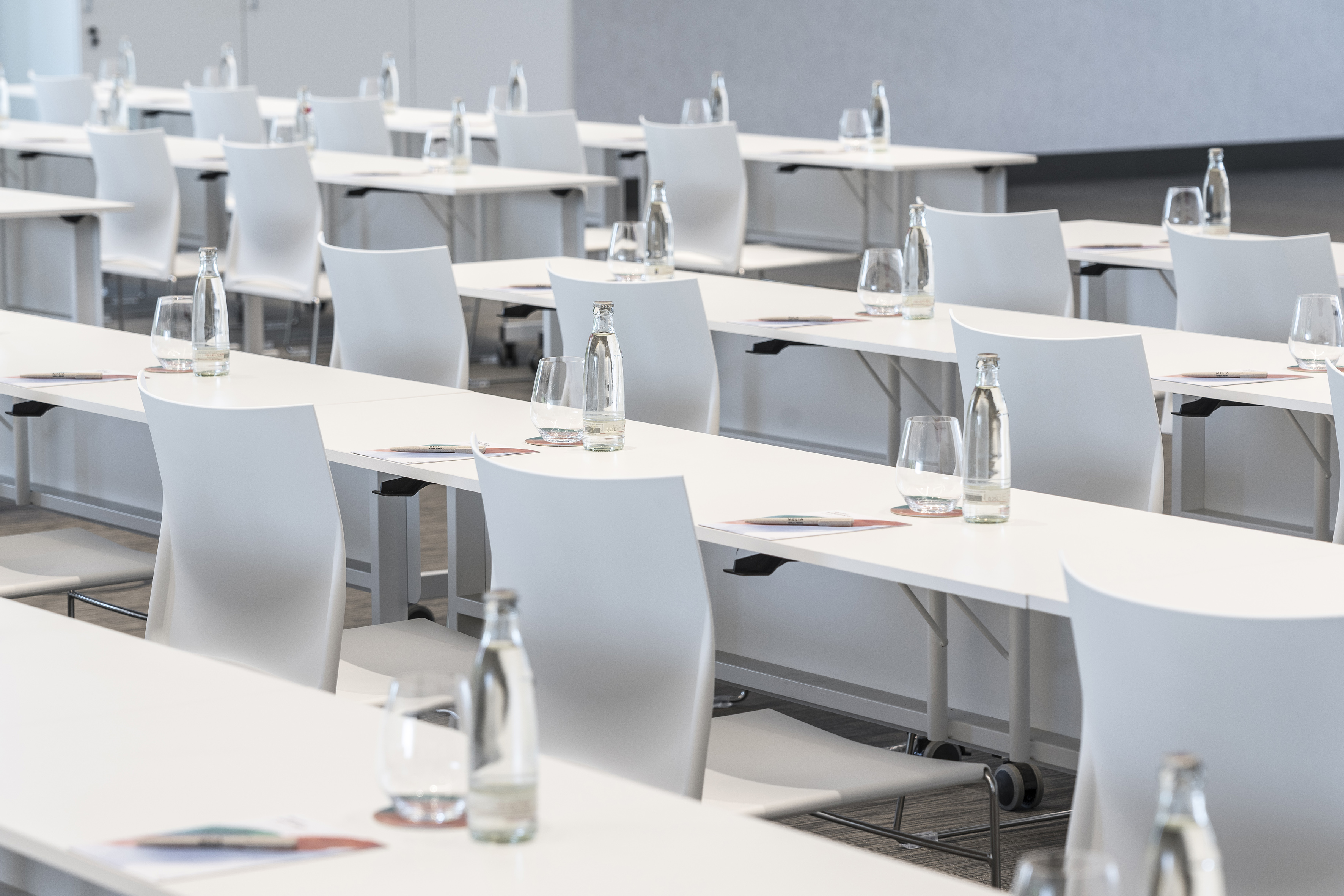 Modern meeting room setup with white tables, chairs, bottled water & glasses.