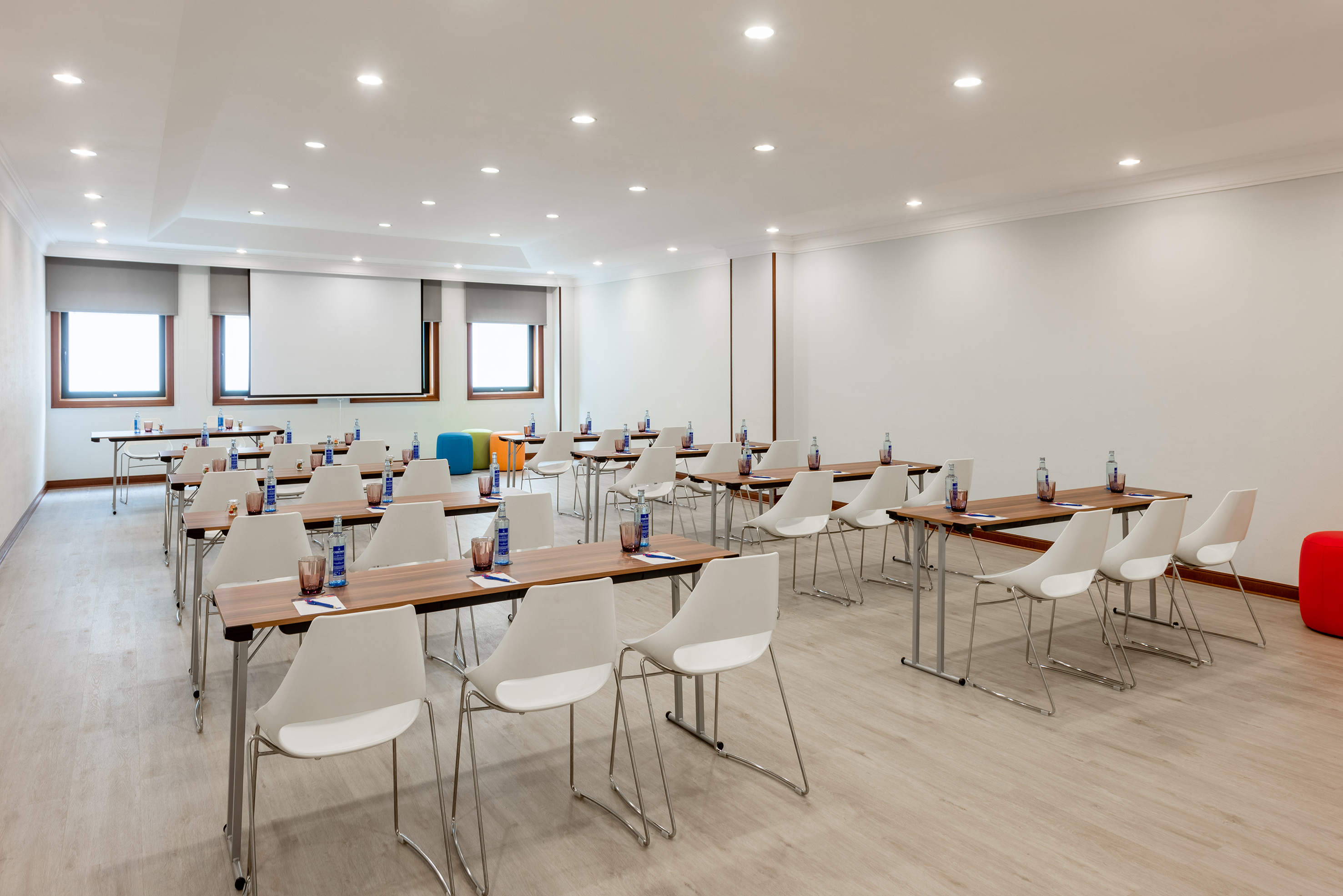 Contemporary hotel meeting room with classroom setup and projection screen.