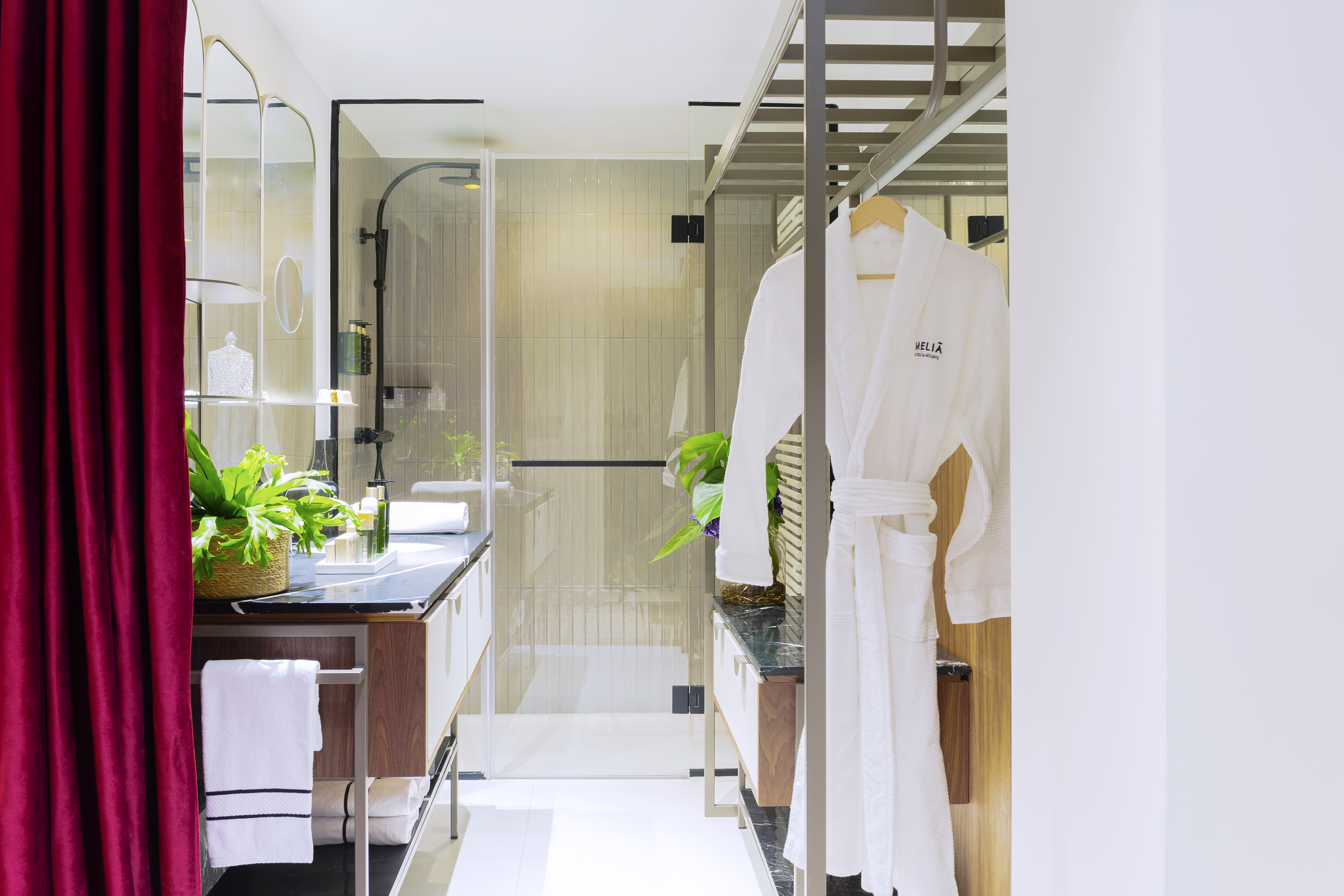 Modern luxury hotel bathroom with walk-in shower, dual vanities, and white bathrobe.