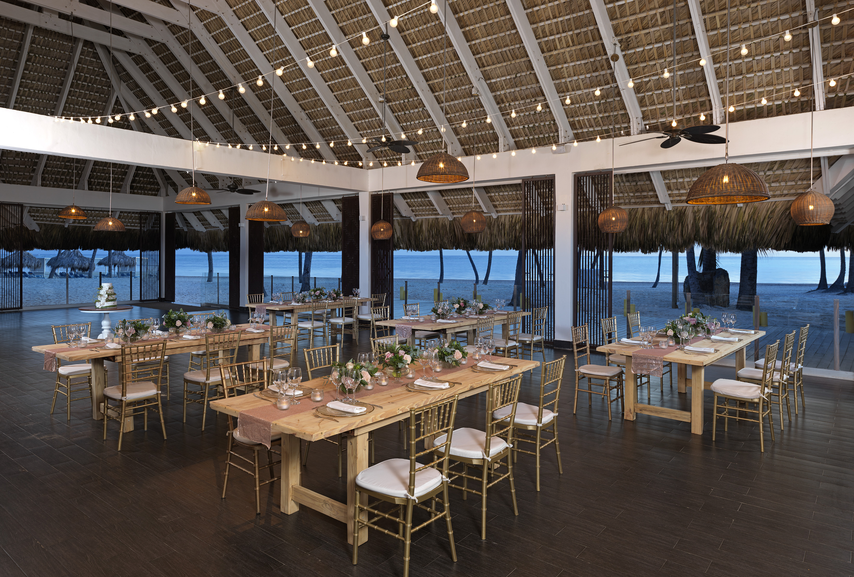 Tropical beachfront wedding venue with dining tables, thatch roof, and ocean view.