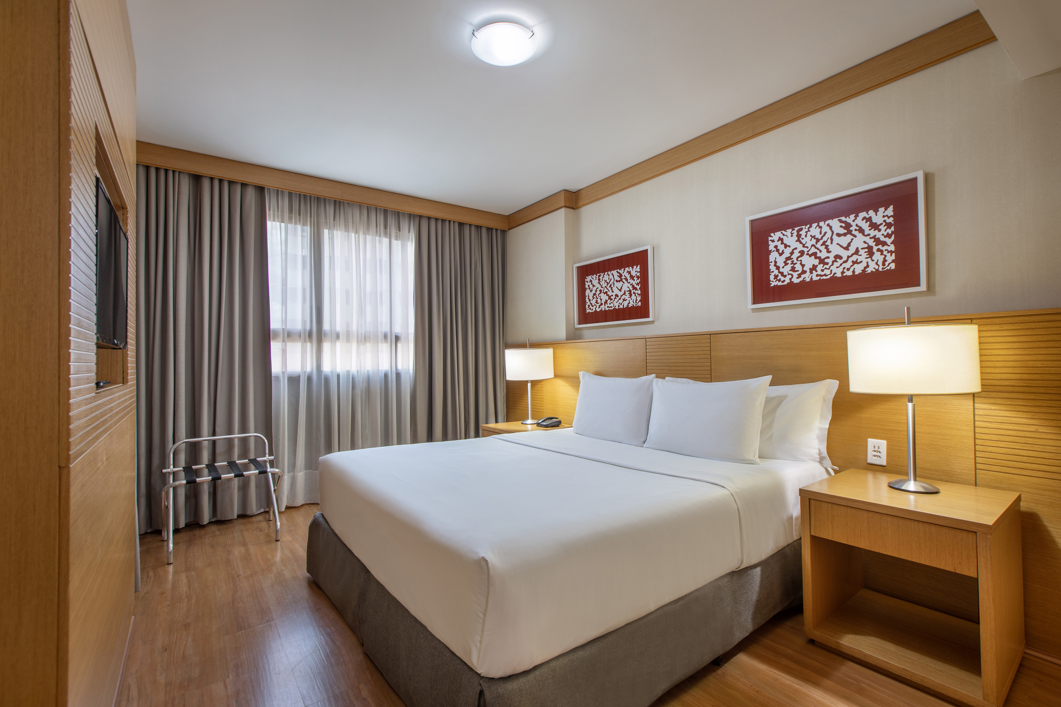Modern hotel room with king bed, wooden headboard, bedside tables, and lamps.