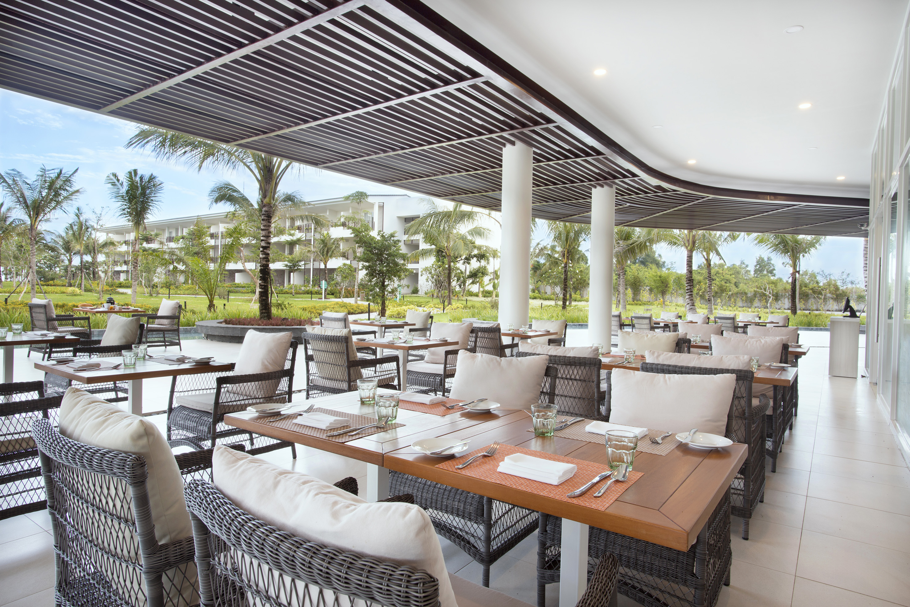 Outdoor resort restaurant with set dining tables and tropical palm trees.