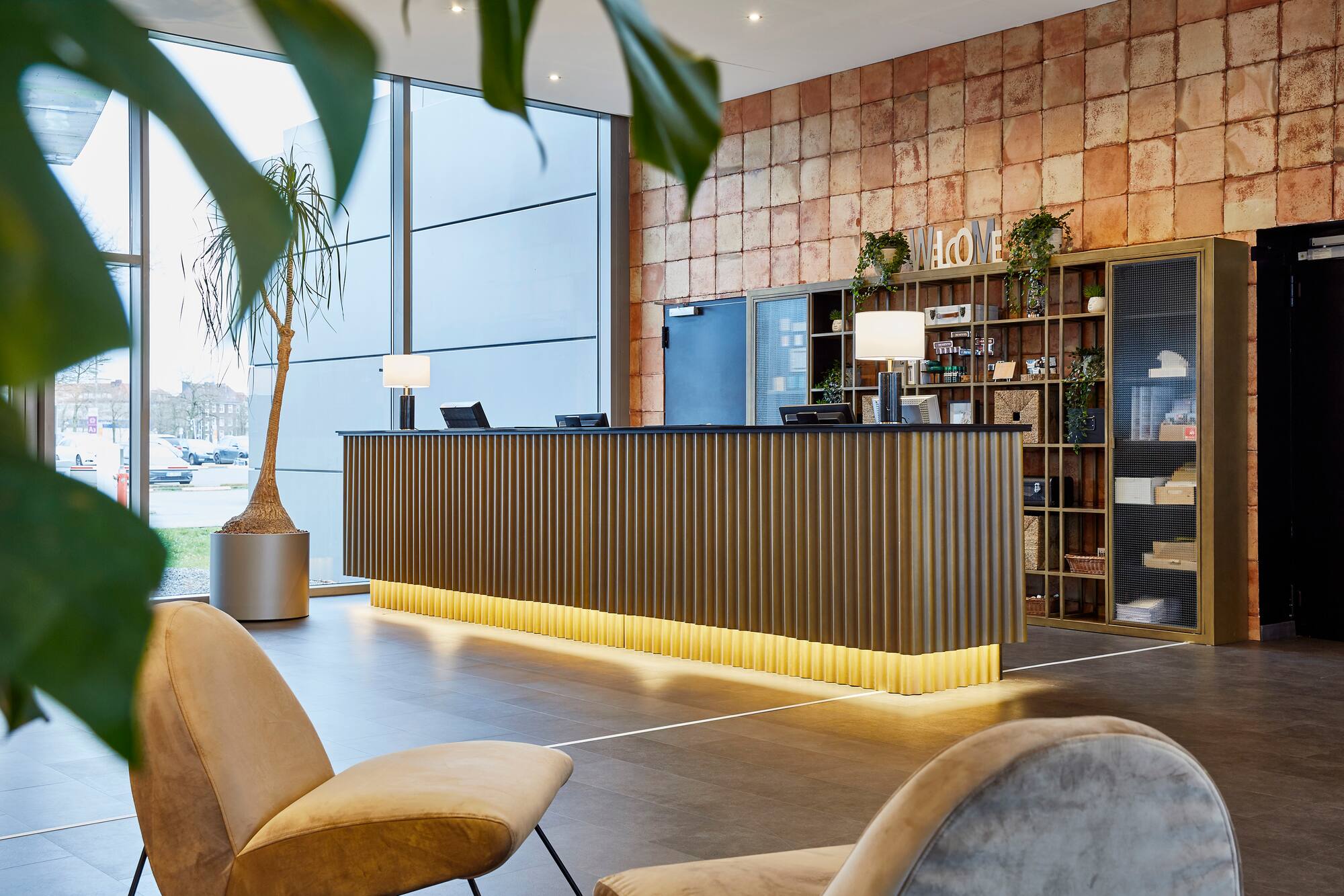 Contemporary hotel lobby with reception desk, brick wall, and lounge seating.