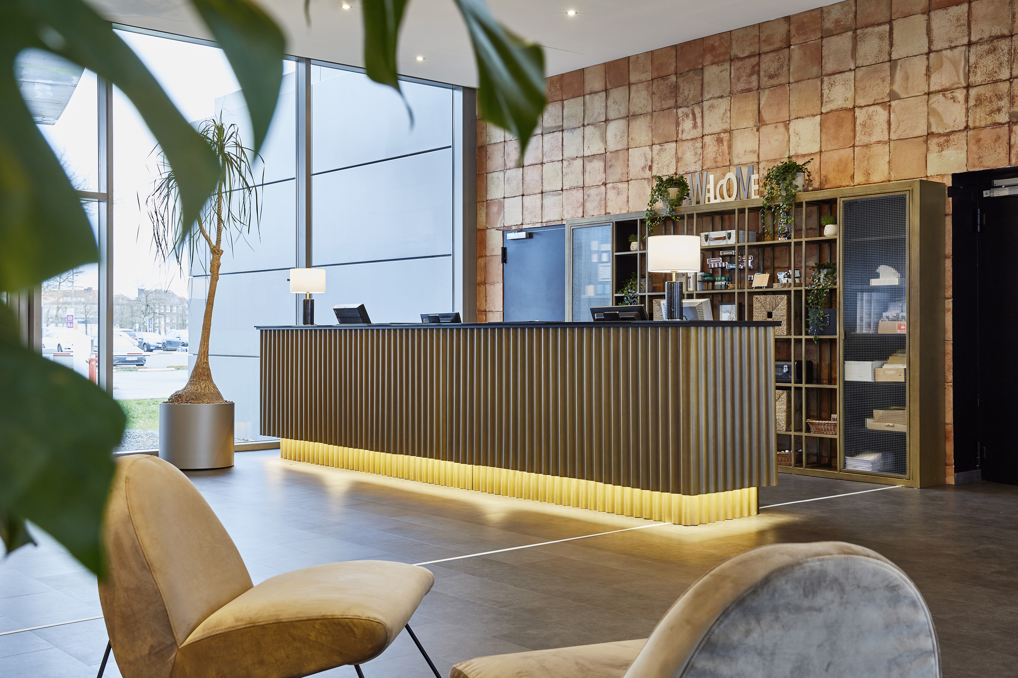 Contemporary hotel lobby with reception desk, brick wall, and lounge seating.