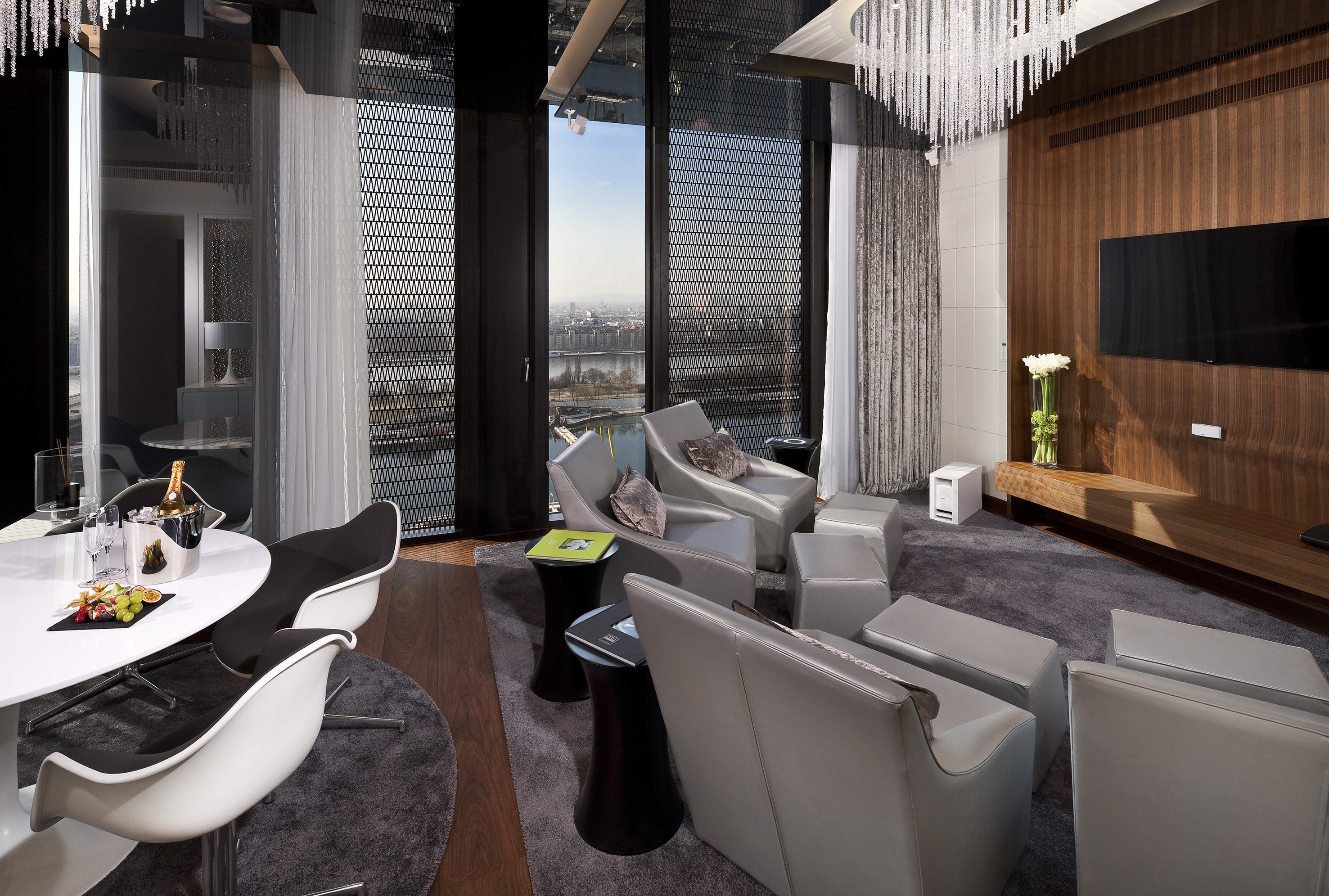 Modern luxury suite interior with cityscape view, grey chairs, and sleek design.