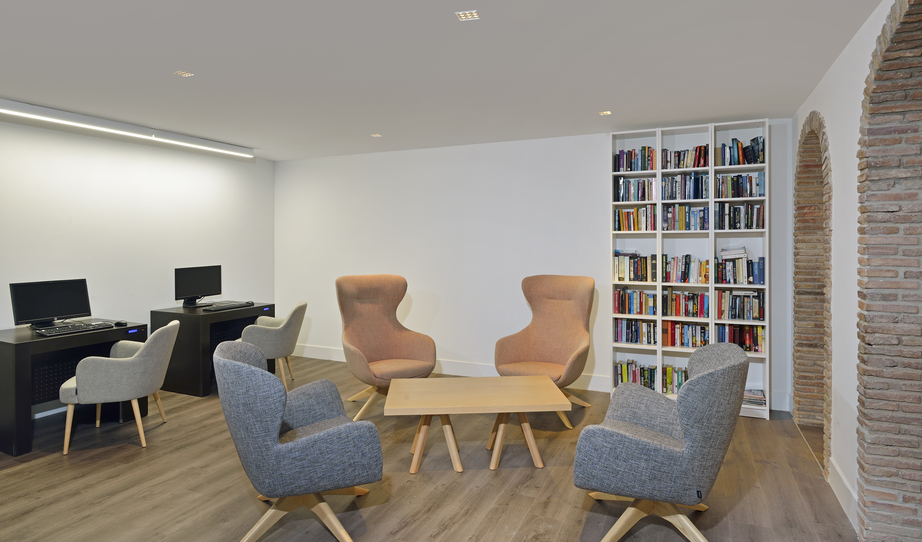 Modern common area with computers, lounge seating, coffee table, and large bookshelf.