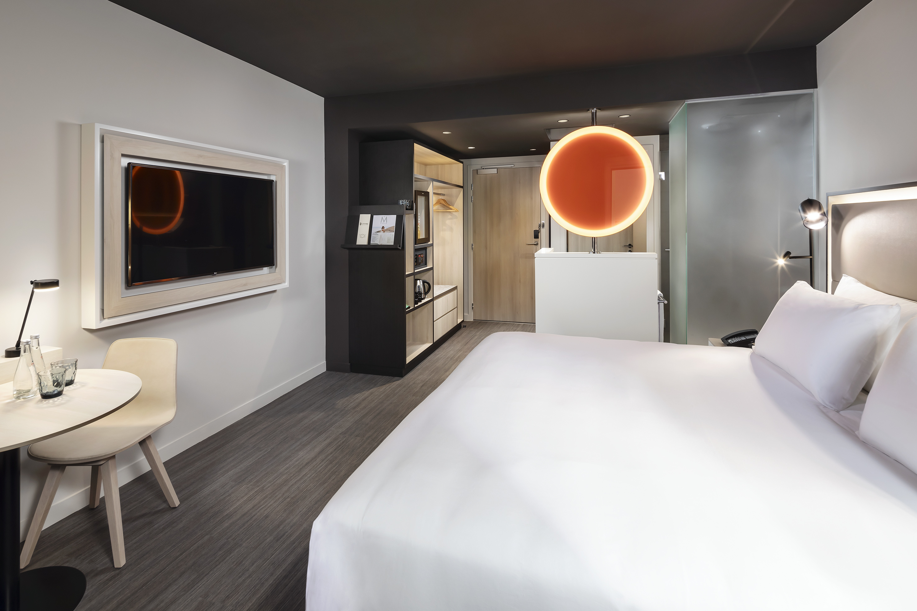 Modern hotel room with large bed, wall TV, sleek desk, and stylish lighting.