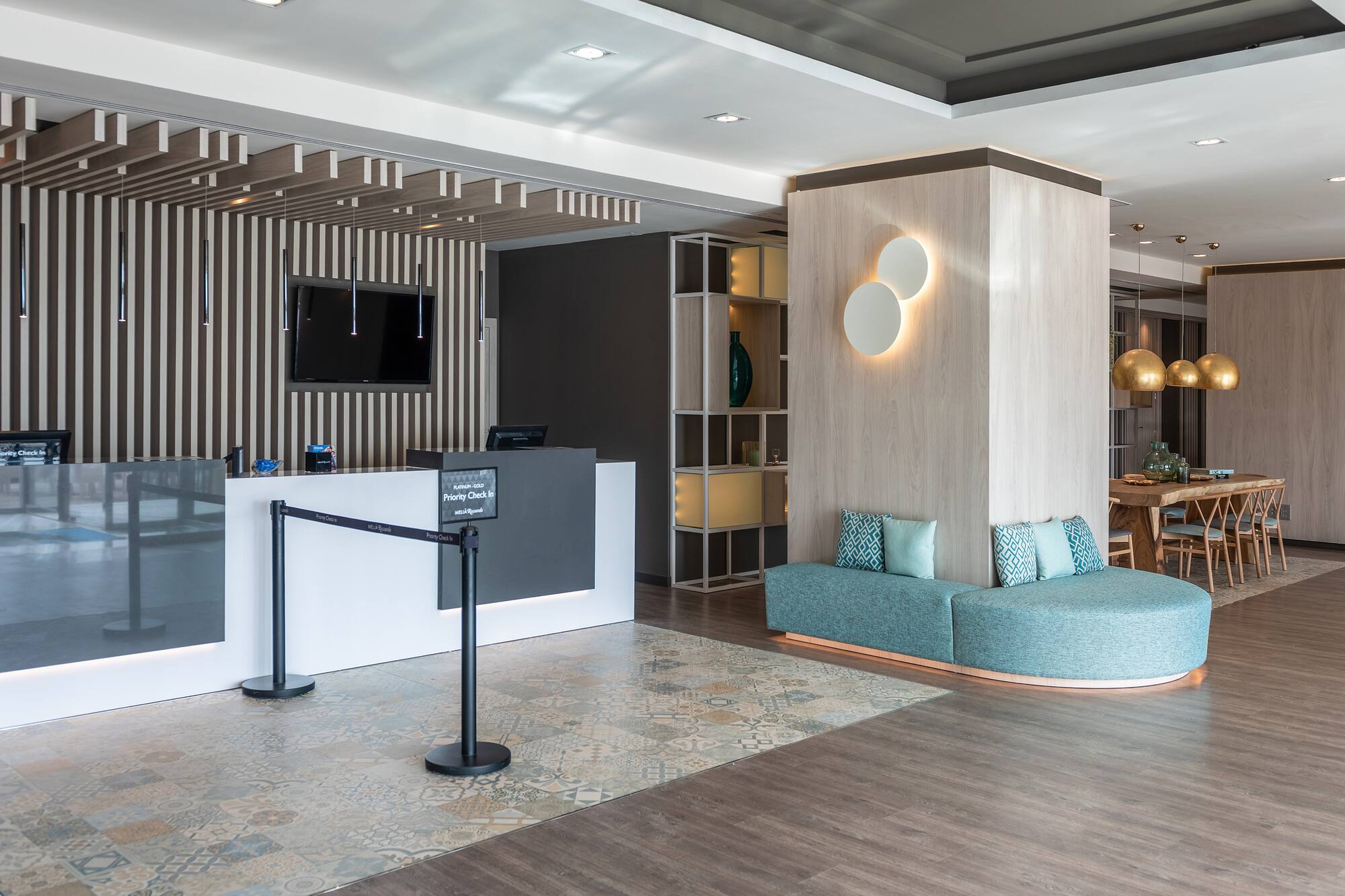 Modern hotel lobby with reception, priority check-in, and teal lounge seating.